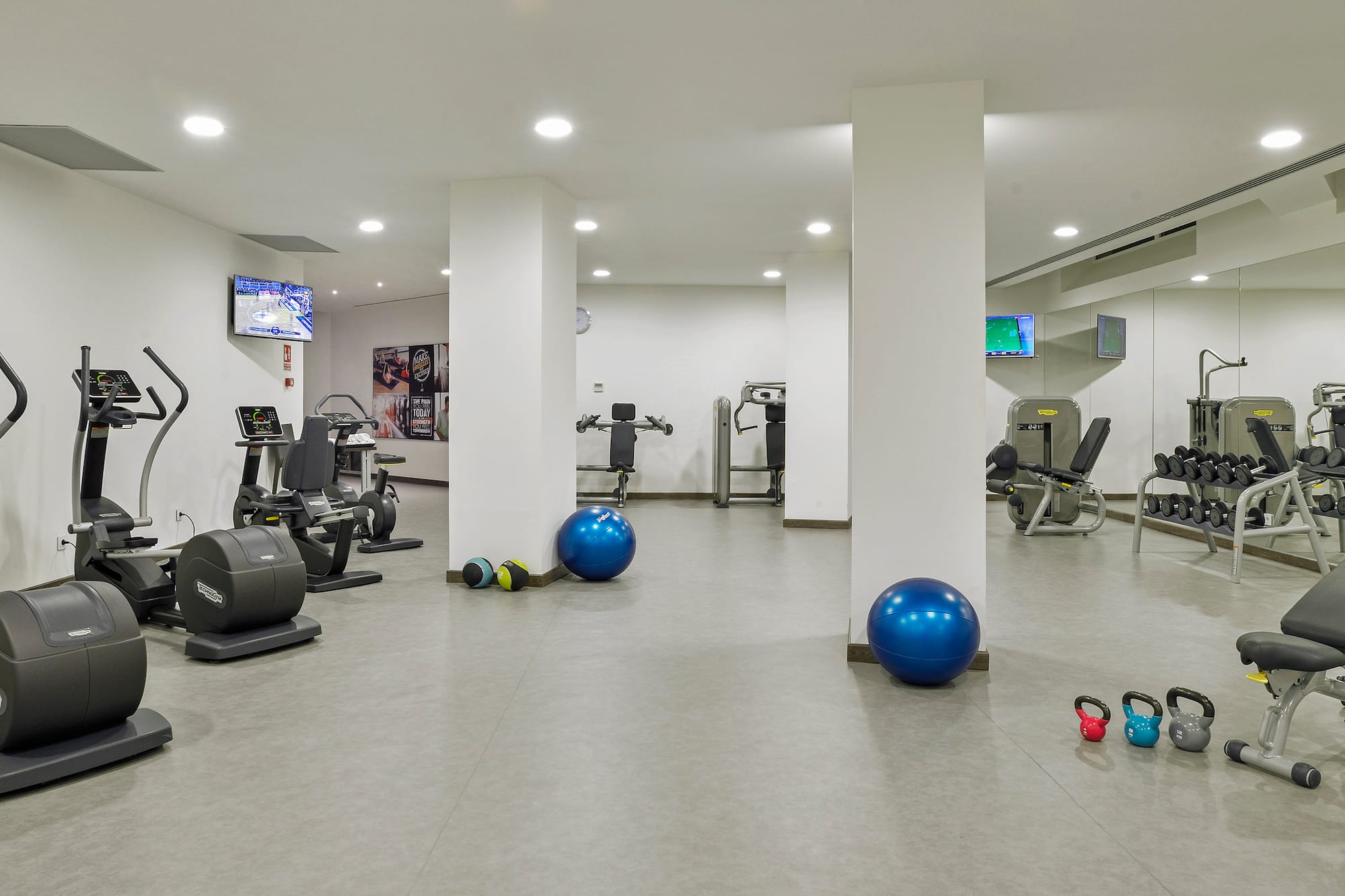 Gimnasio moderno con máquinas de cardio, pesas, y balones de ejercicio.