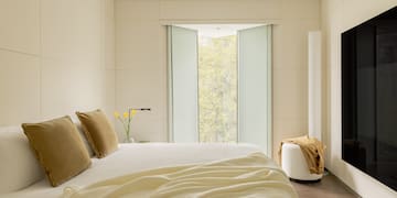 a bed with pillows and a vase of flowers in front of a window