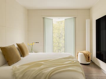 a bed with pillows and a vase of flowers in front of a window