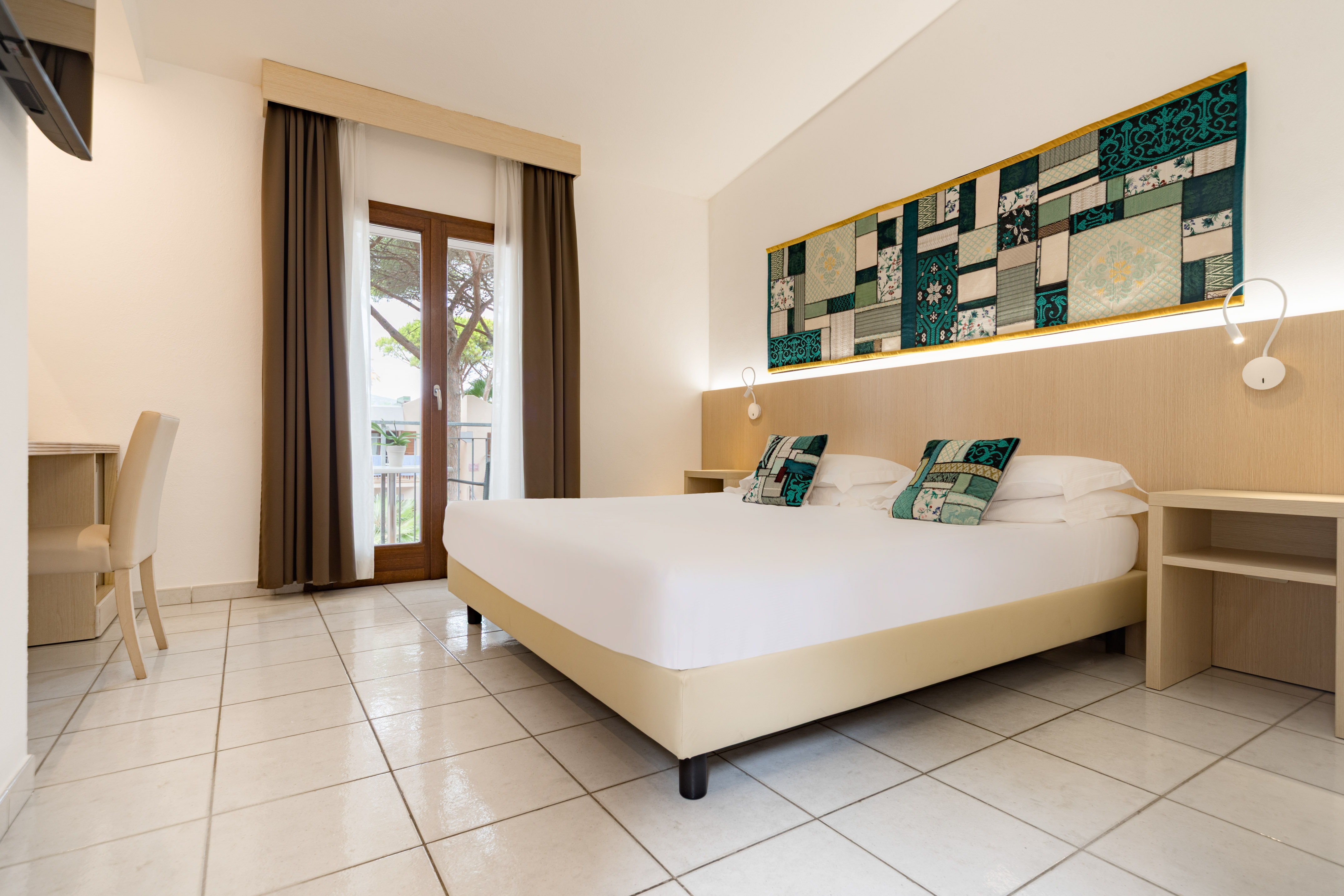 Spacious hotel bedroom with a queen bed, balcony, and patterned wall decor.