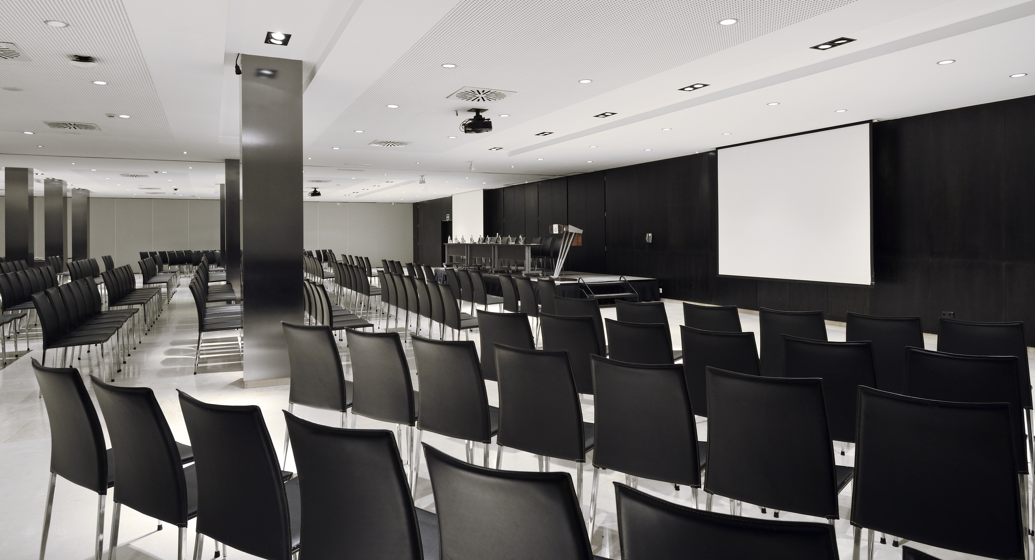 Empty modern conference room with black chairs, stage, and projection screen.