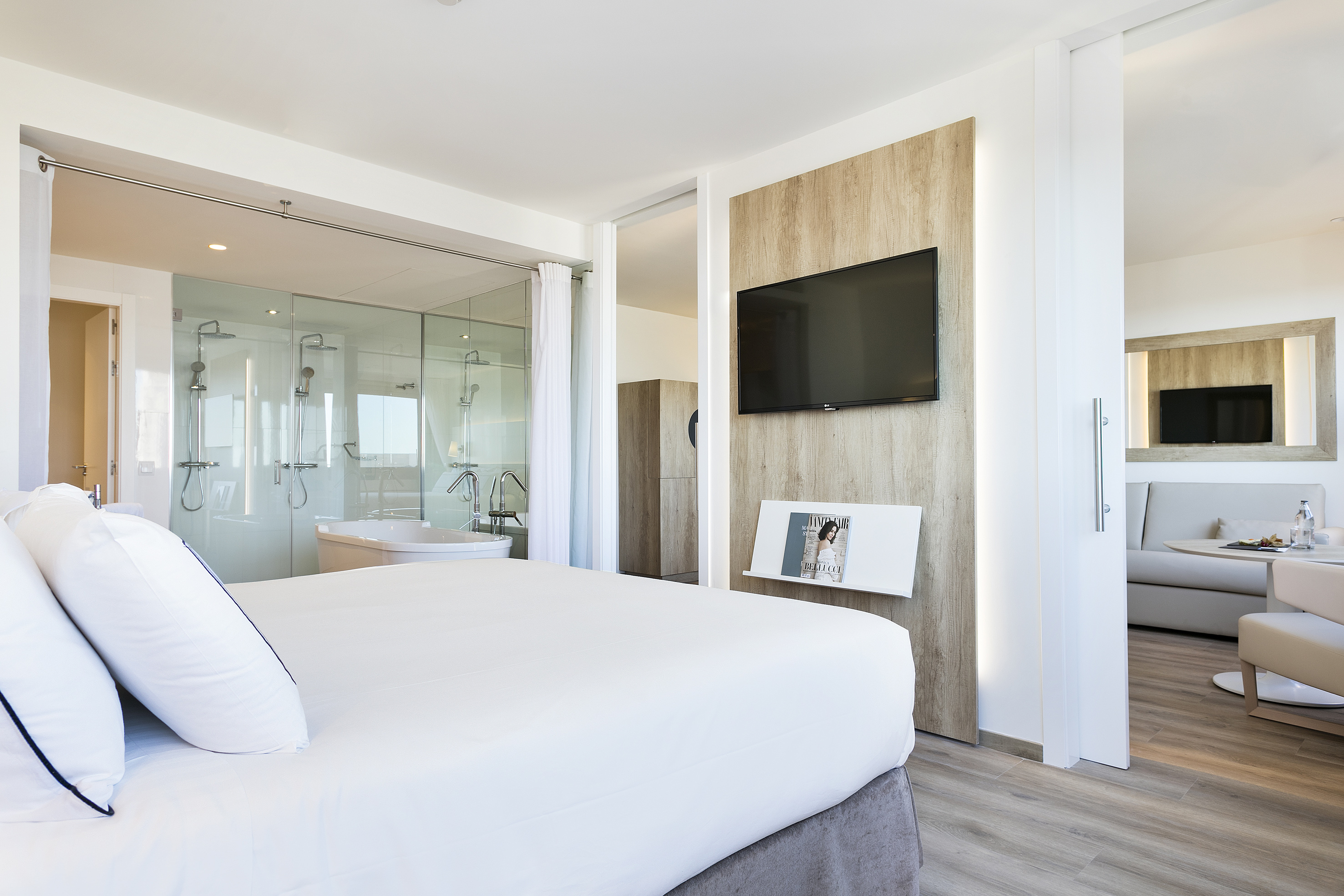 Spacious modern hotel suite with glass bathroom and living area.
