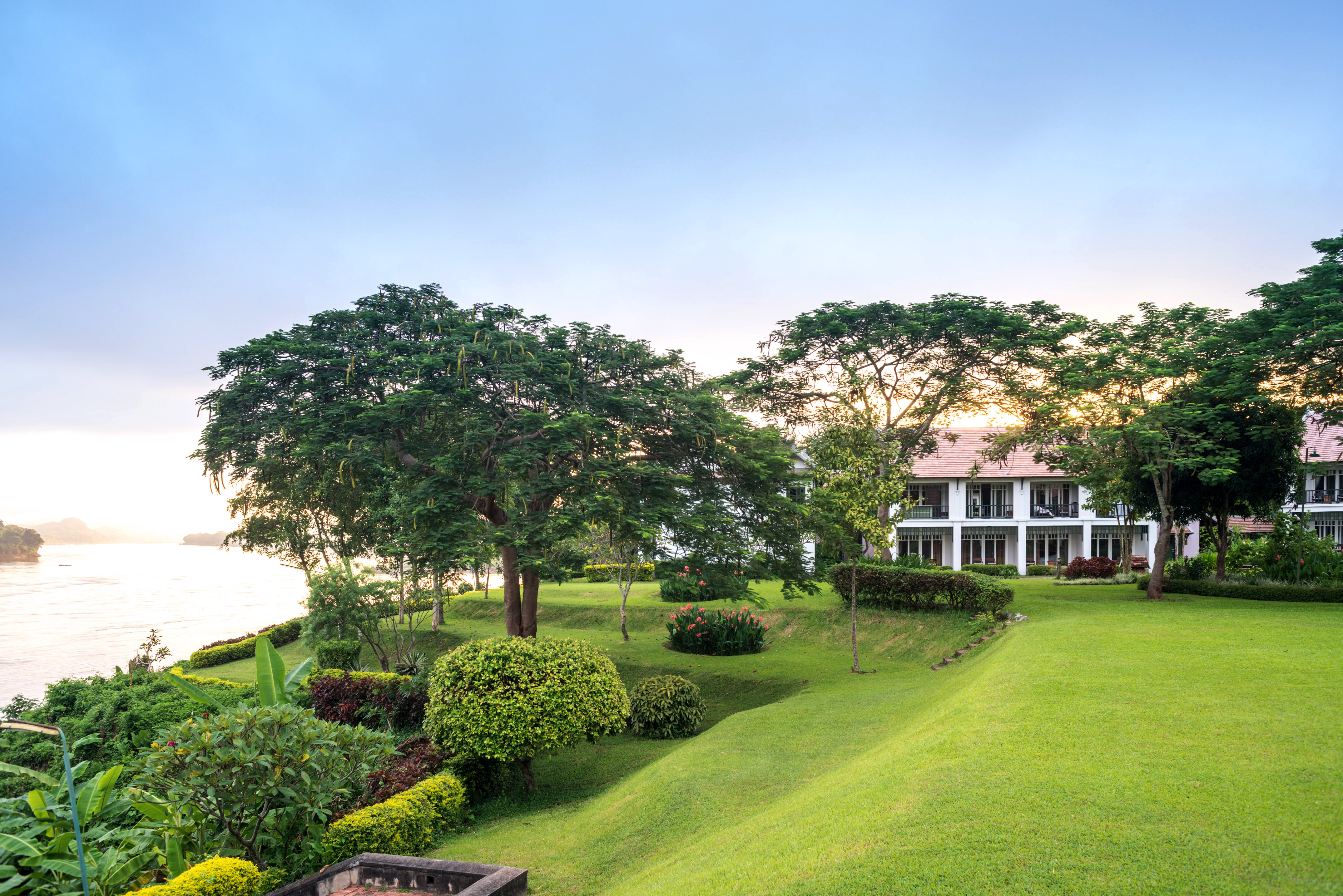 Tropical riverside resort with lush lawn and trees under blue sky.