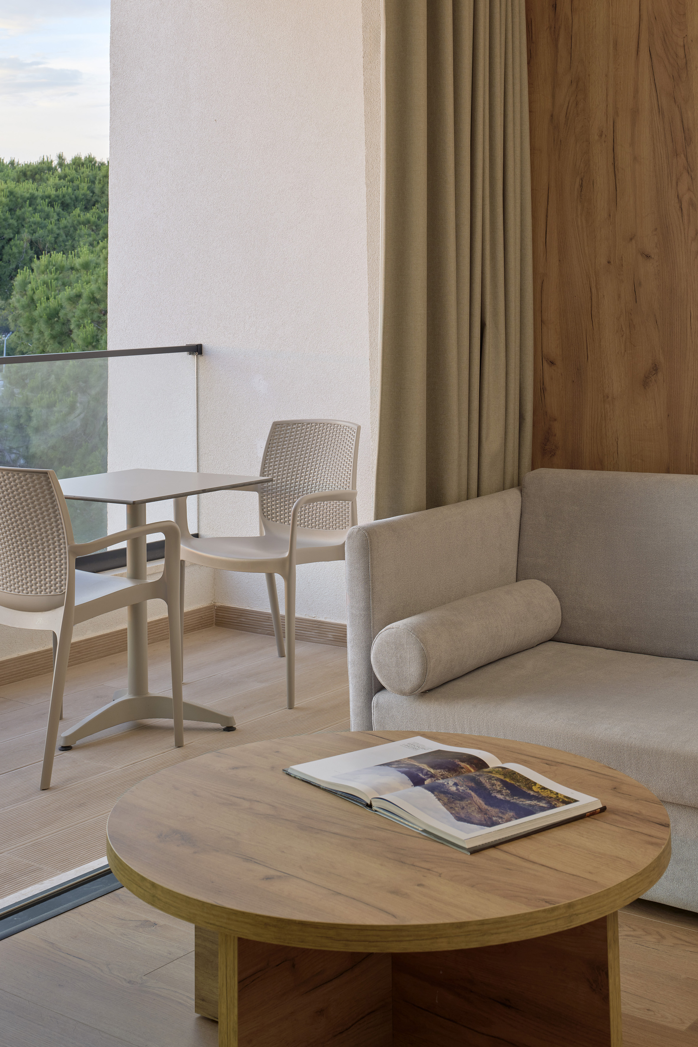 Modern hotel room with balcony, sofa, round coffee table, and outdoor chairs.