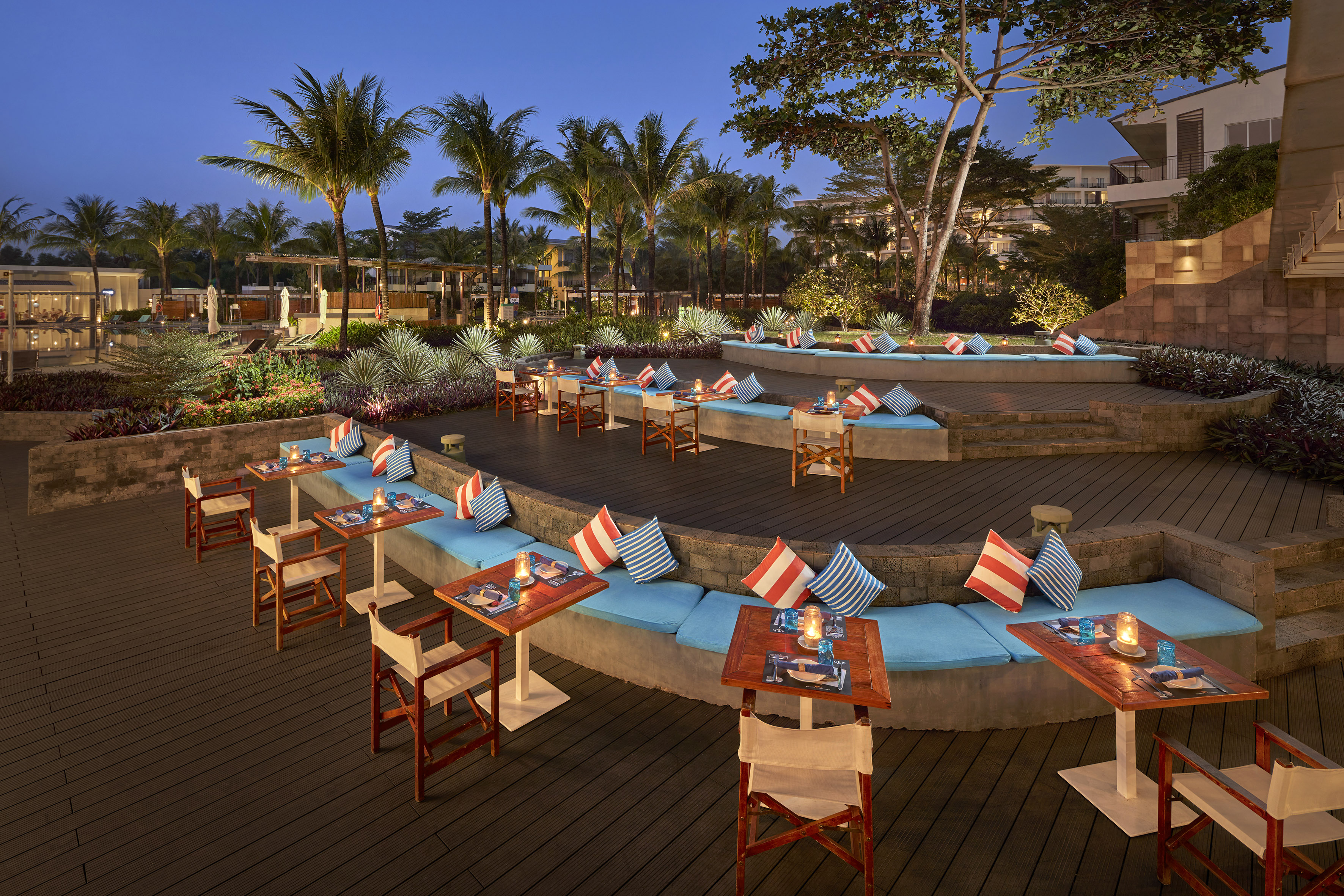 Nighttime outdoor dining at a tropical resort with blue benches and palm trees.
