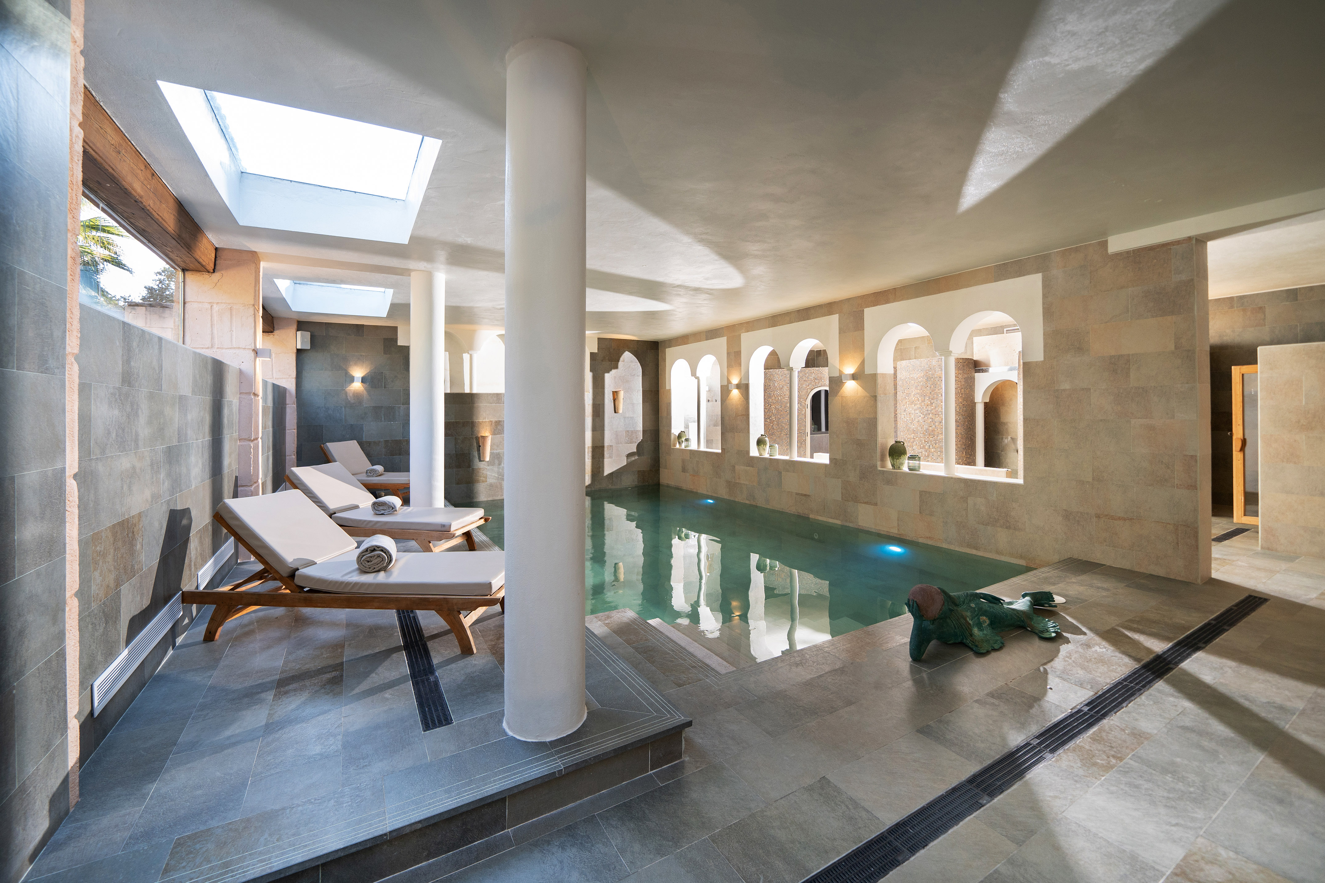 Elegant indoor spa pool with skylights, stone tiles, and lounge chairs.