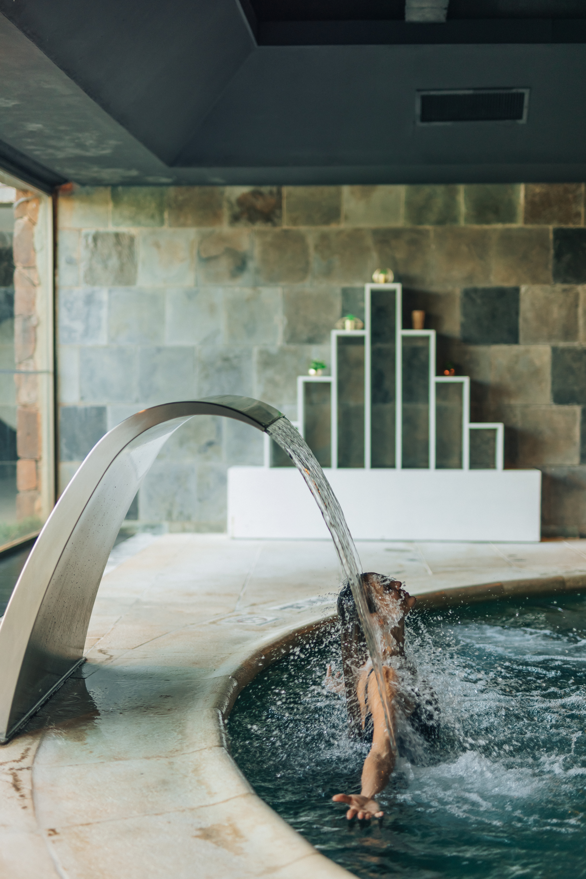 Woman experiencing hydrotherapy under a modern water jet in a spa hot tub.