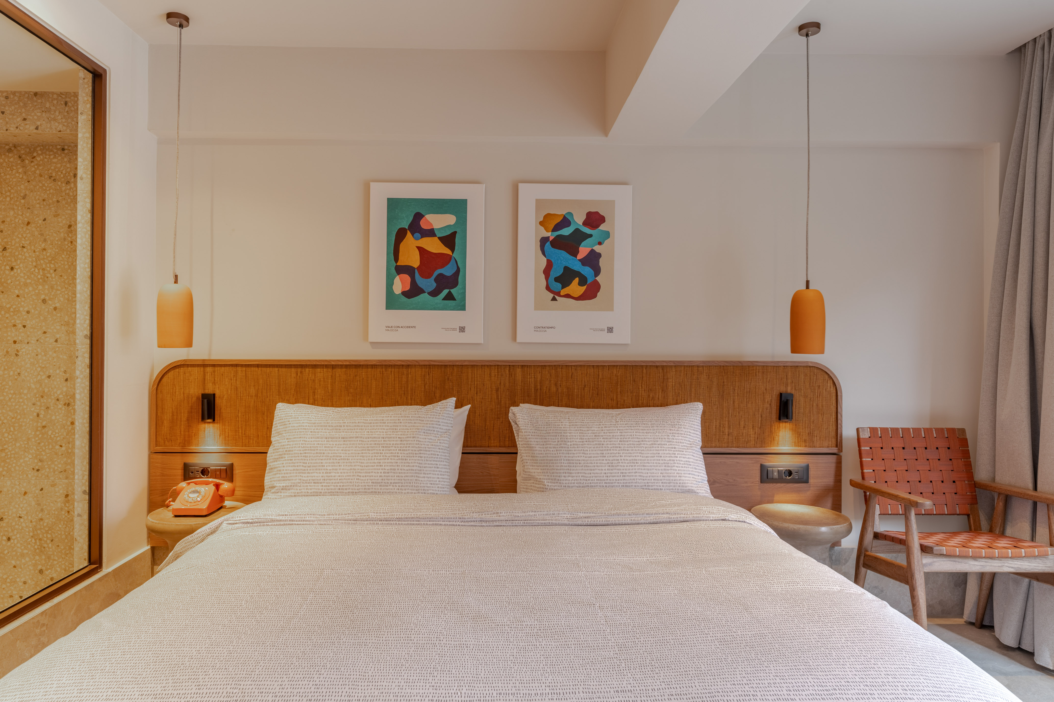 Stylish hotel bedroom, woven headboard, abstract art, orange pendant lights.