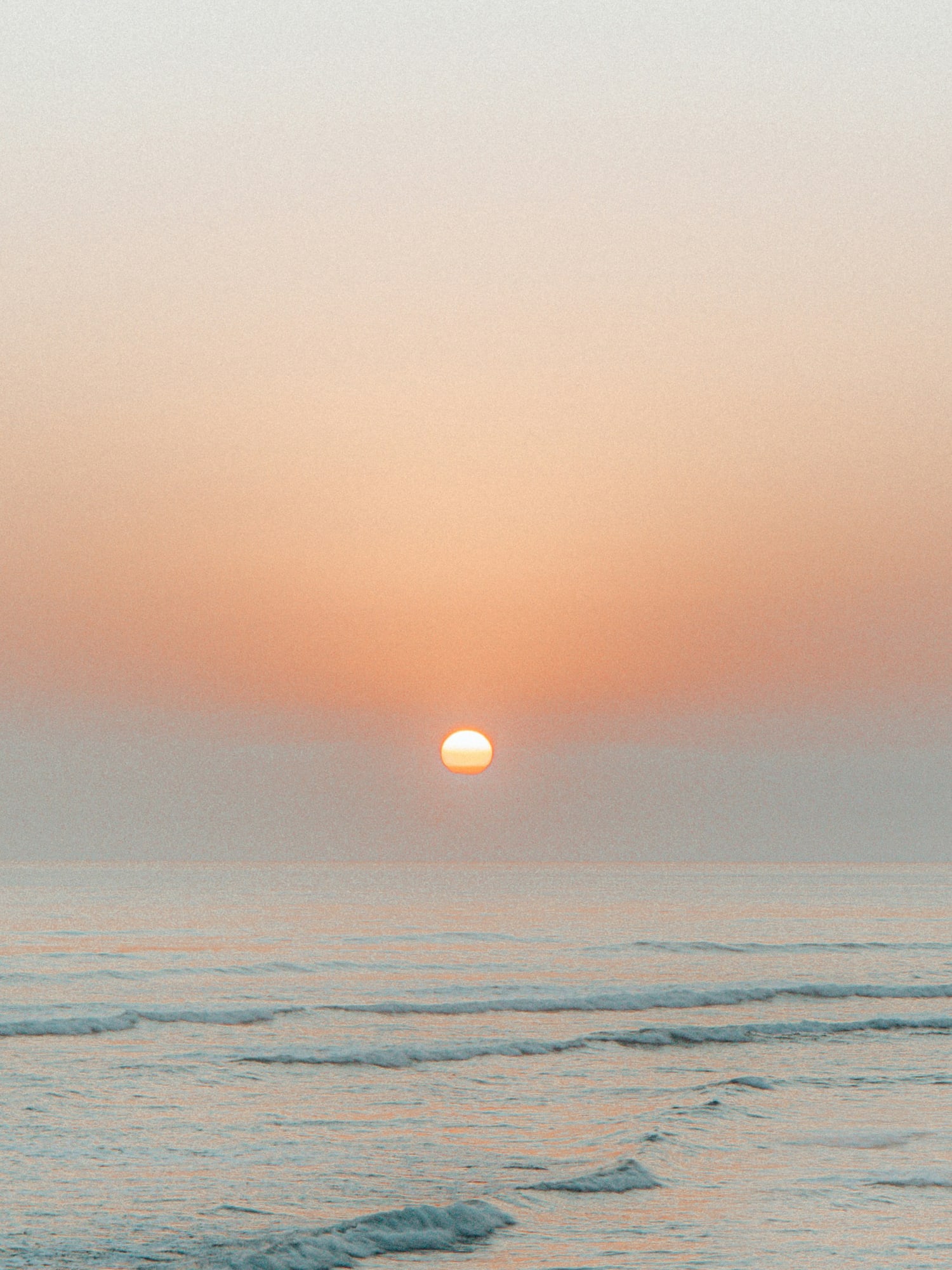 Golden sunset over ocean waves, bright sun low on the horizon.