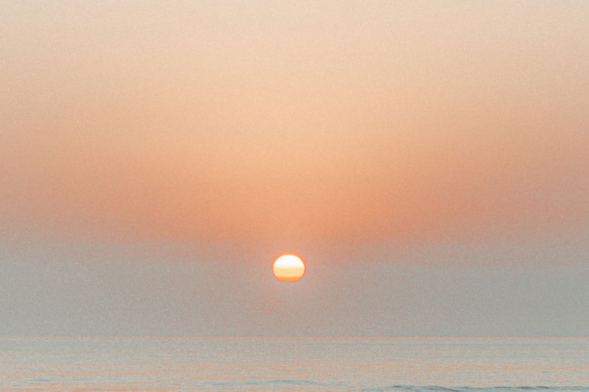 Golden sun setting over calm ocean waves and pastel sky.