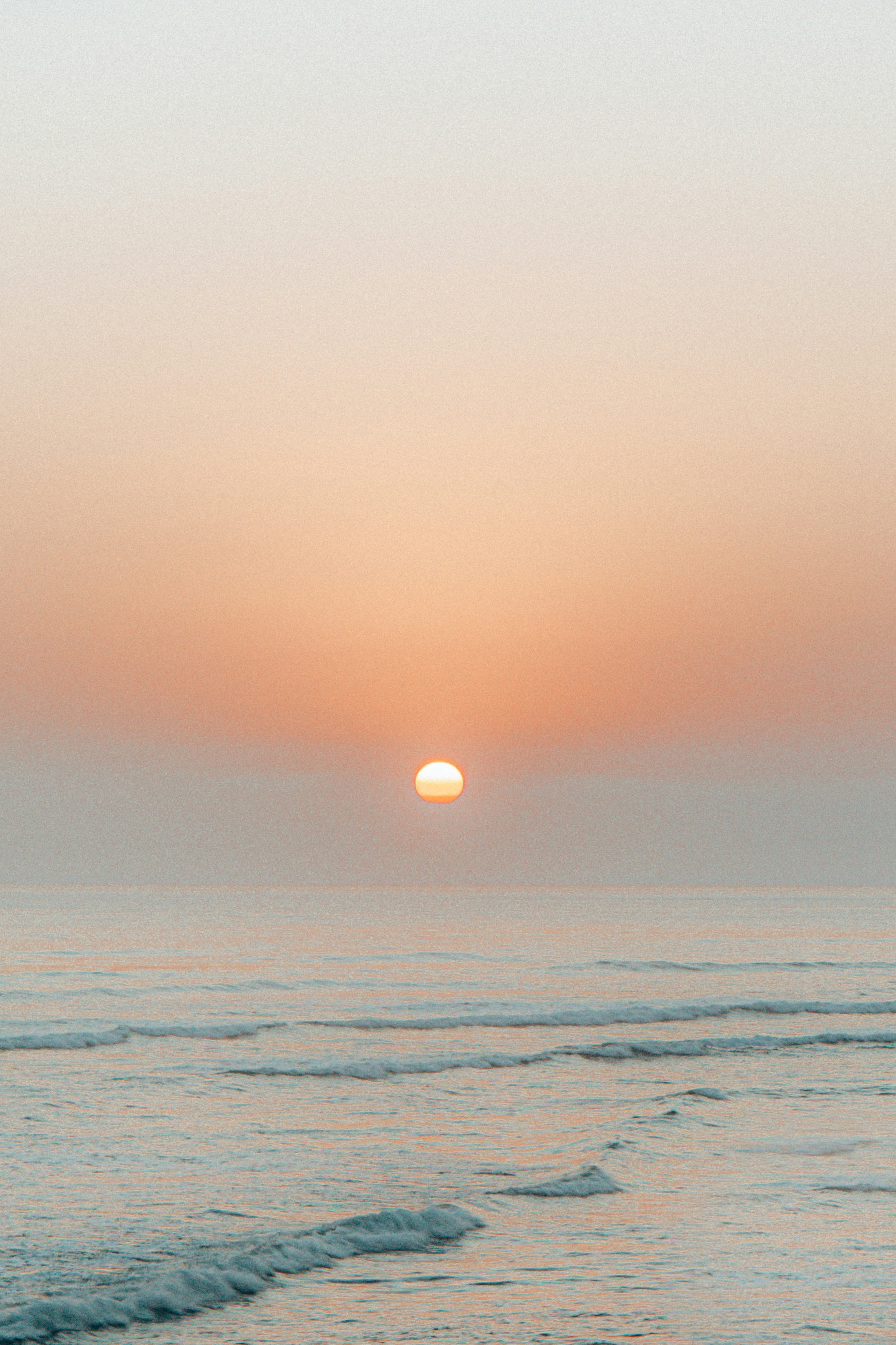 Golden sun setting over calm ocean waves and pastel sky.