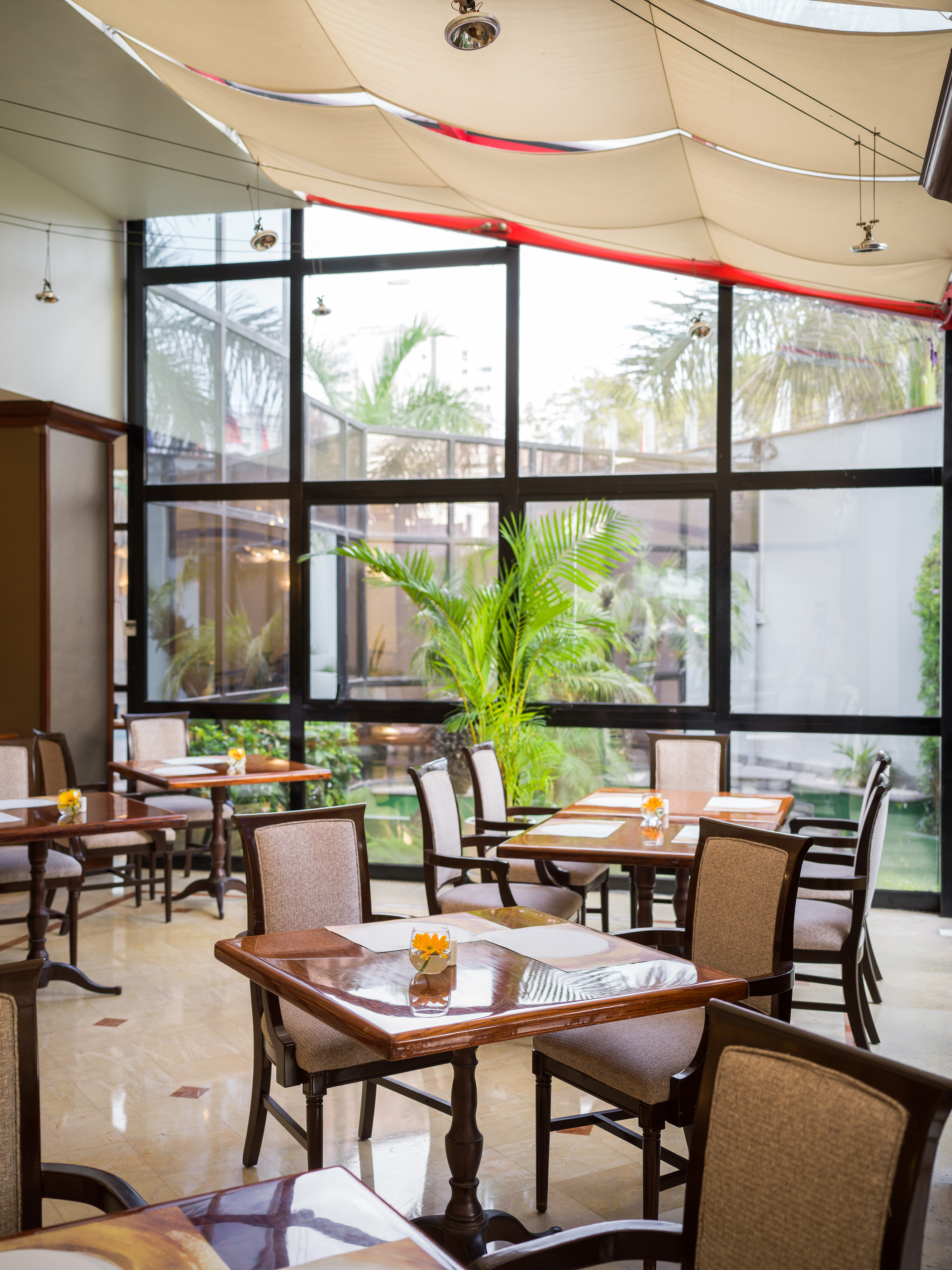 Bright restaurant interior, elegant tables, large windows, and garden view.