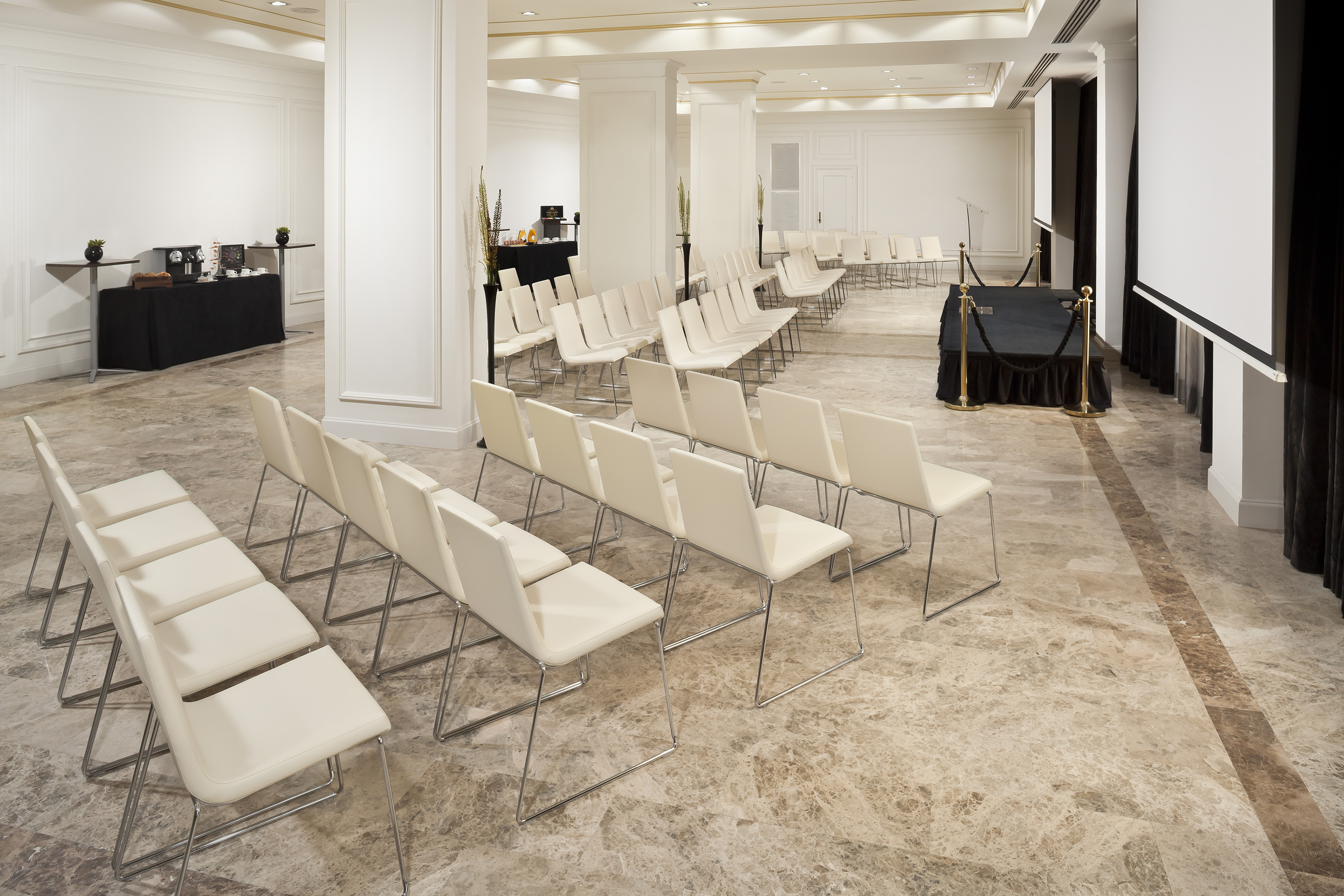 Hotel meeting room with rows of chairs, screen, podium, coffee station.