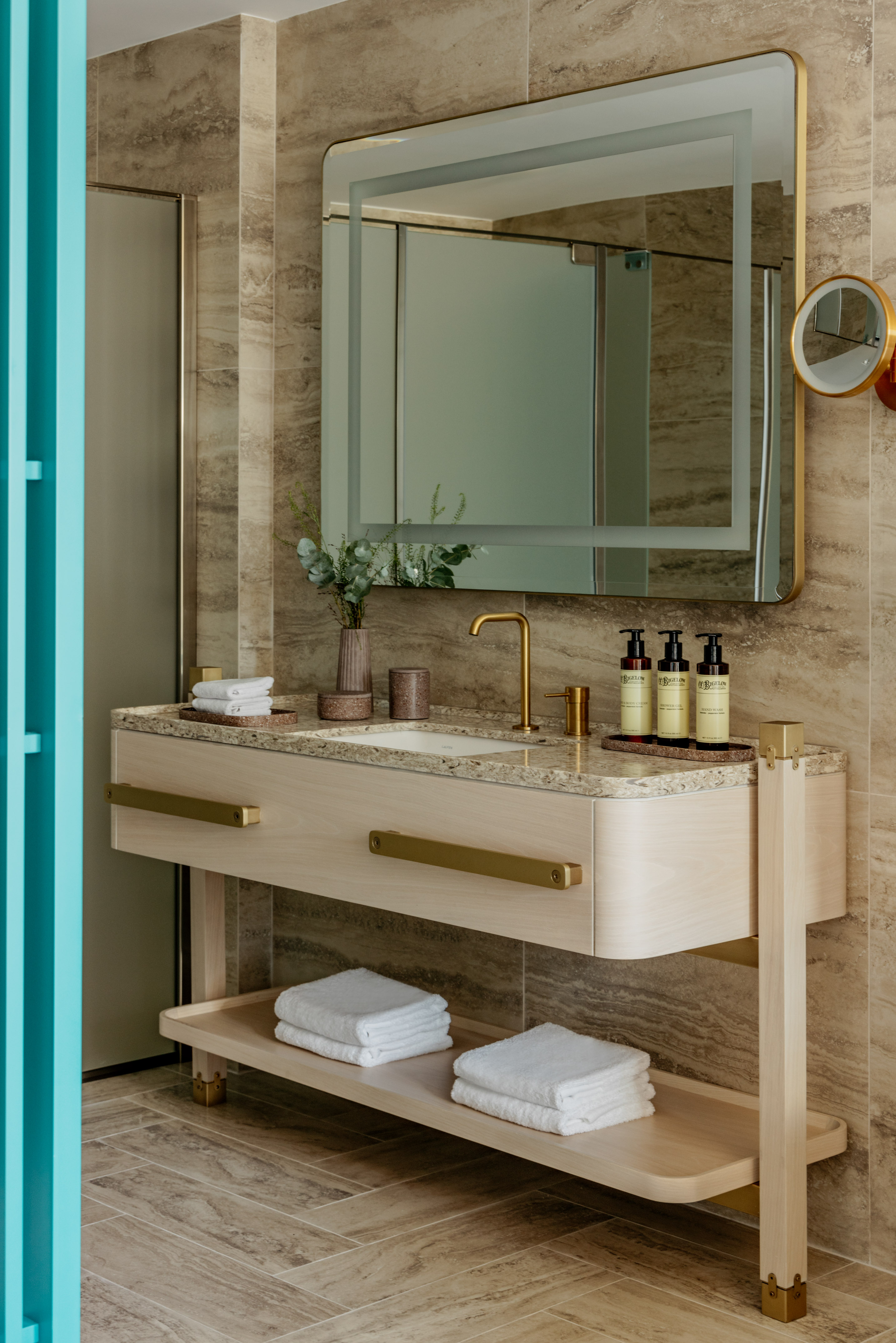 Modern hotel bathroom vanity with gold fixtures, marble, wood cabinet, and mirror.