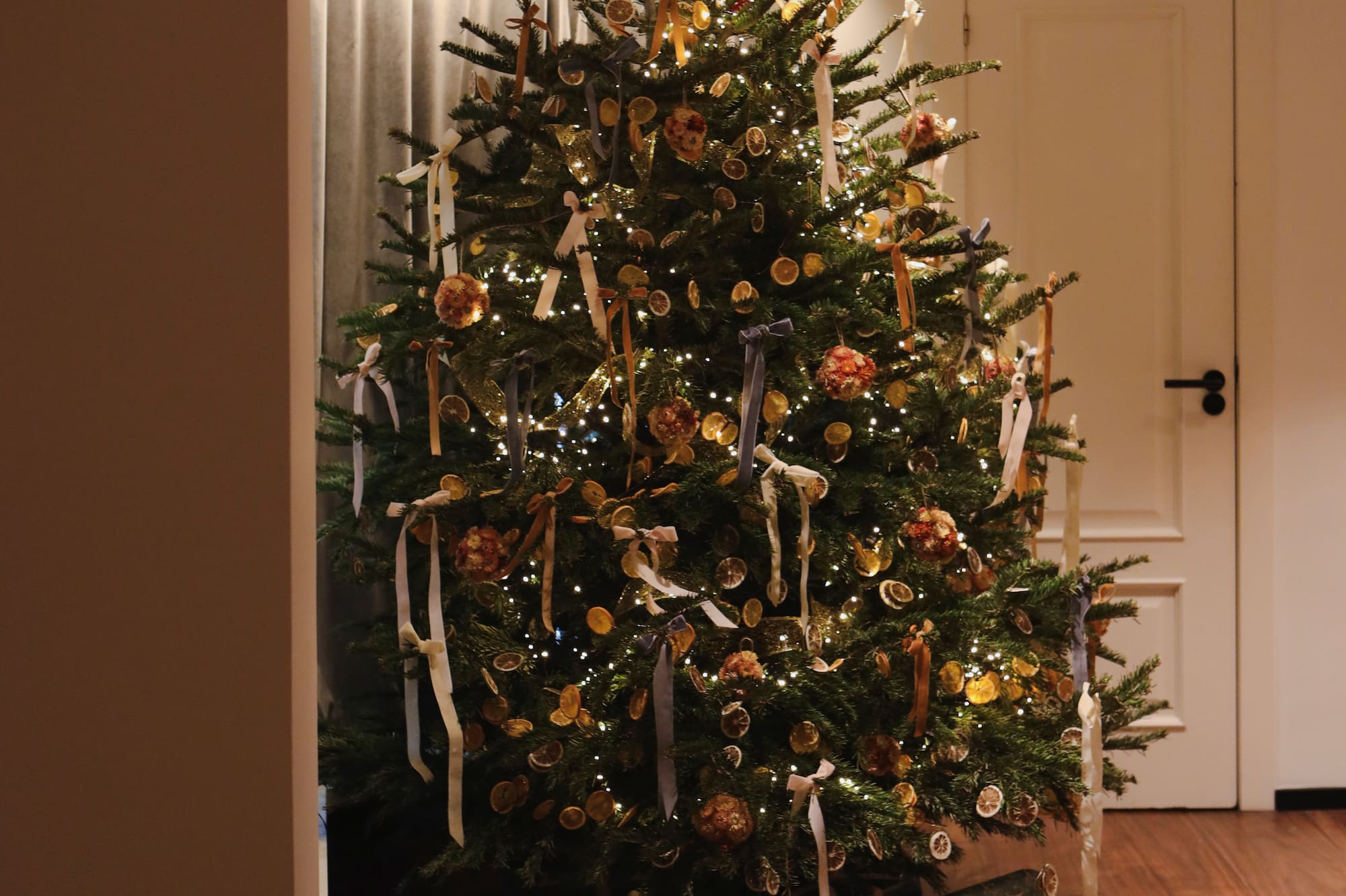 Festive Christmas tree decorated with lights, dried oranges, ribbons, and gifts.