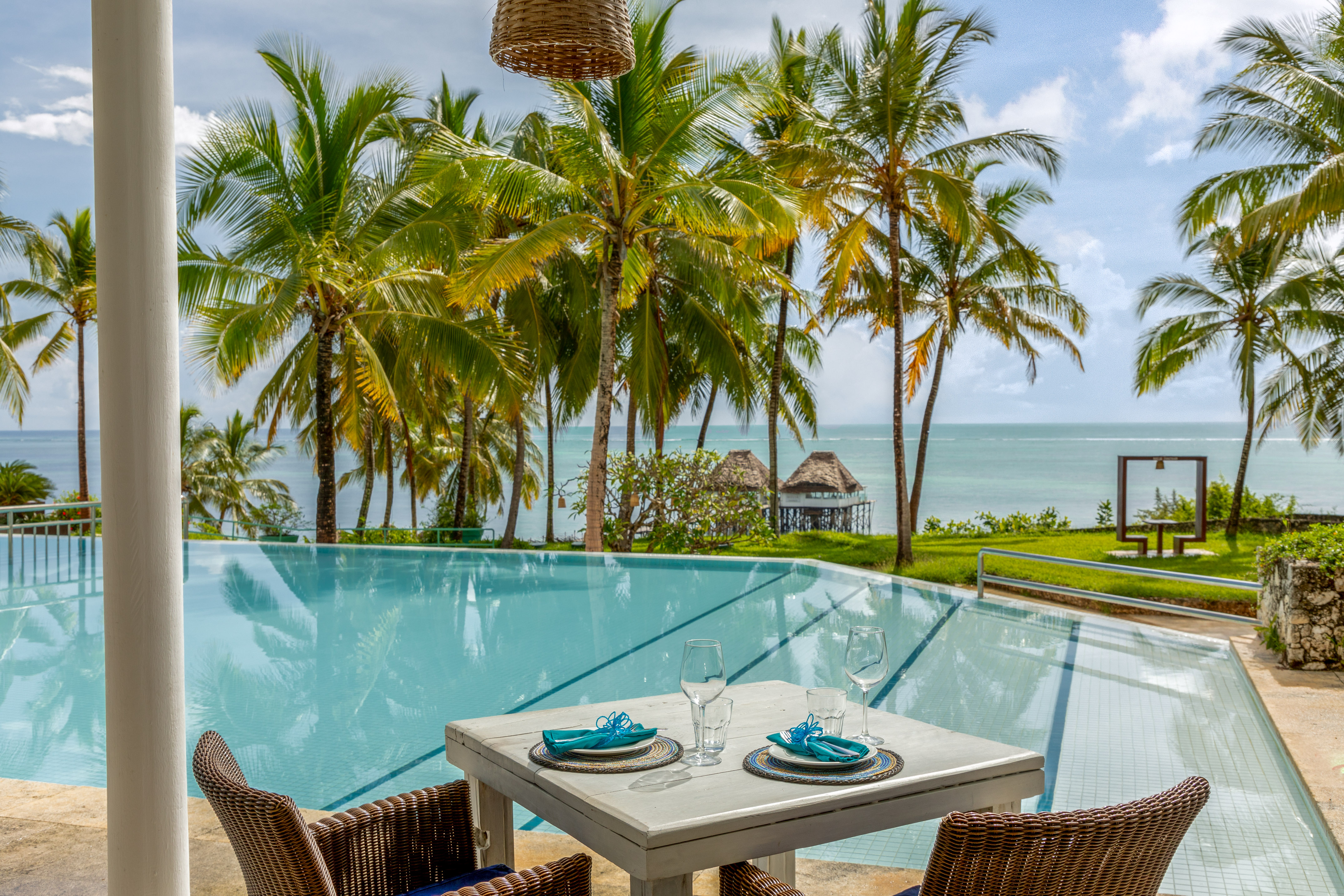 Tropical resort dining by infinity pool with ocean and palm trees.