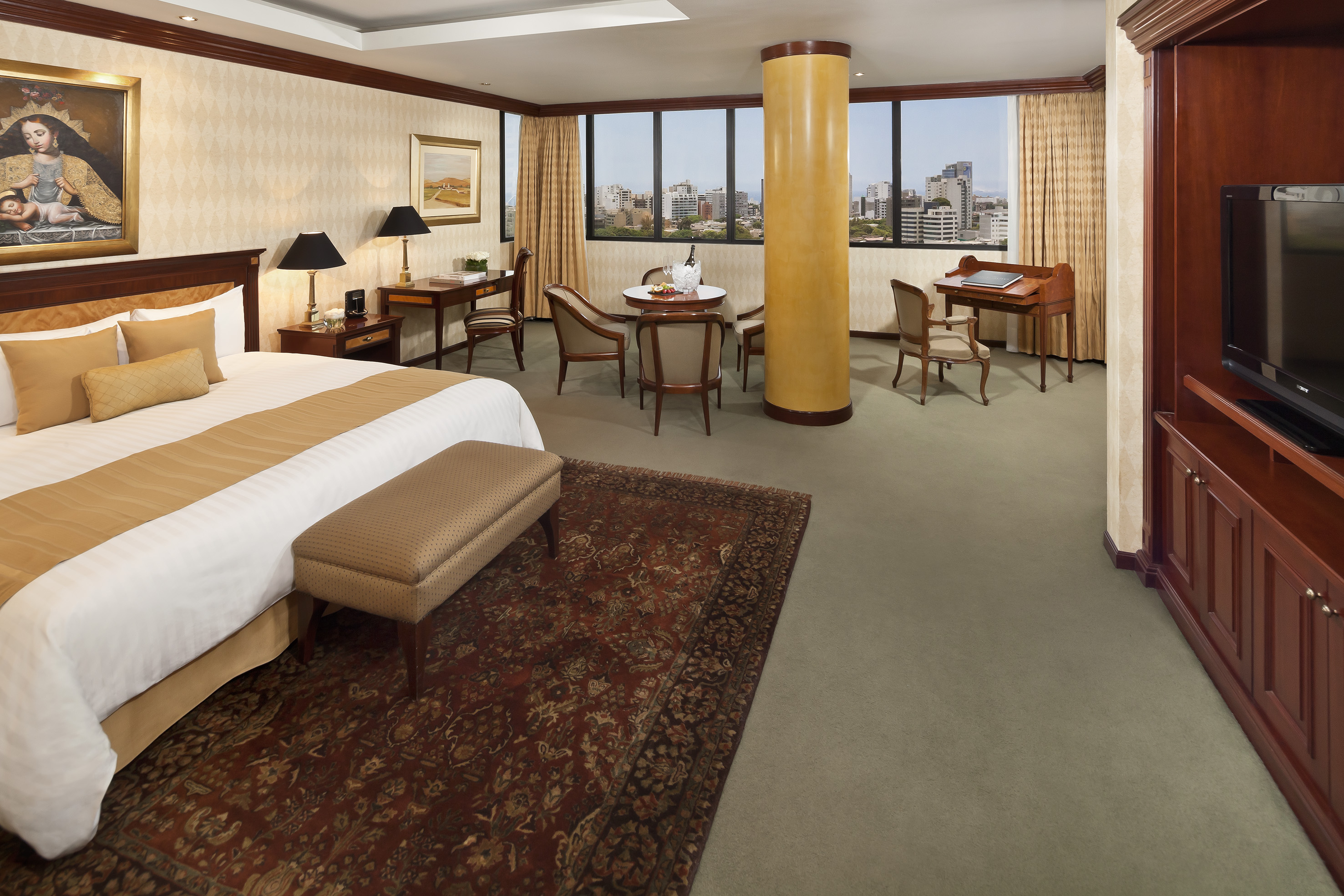 Luxury hotel suite with king bed, city view, work desk, and dining table.