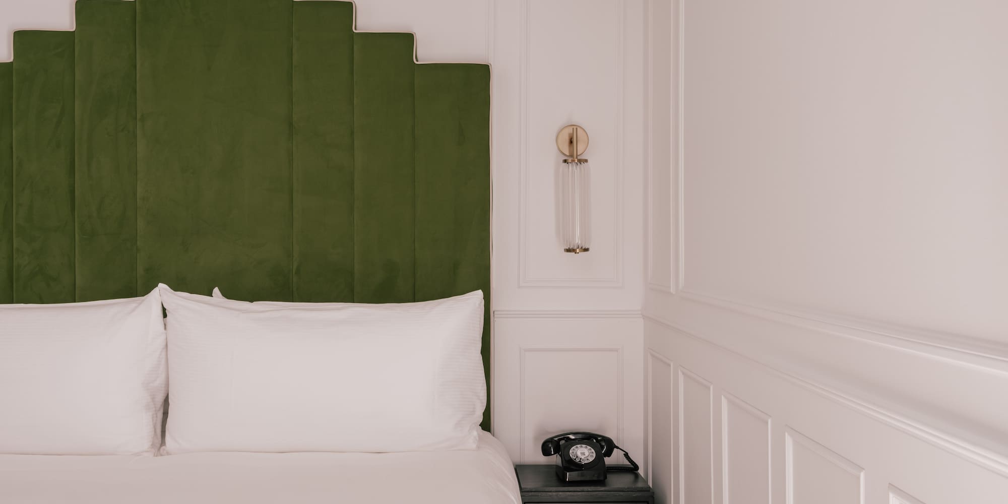 Green velvet geometric headboard, white bed, vintage phone, modern hotel room.