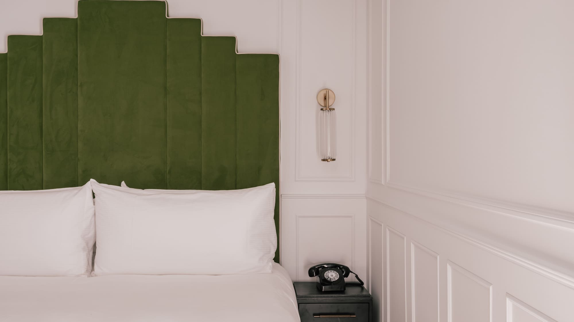Luxurious hotel room with green velvet headboard, white bed, and vintage phone.