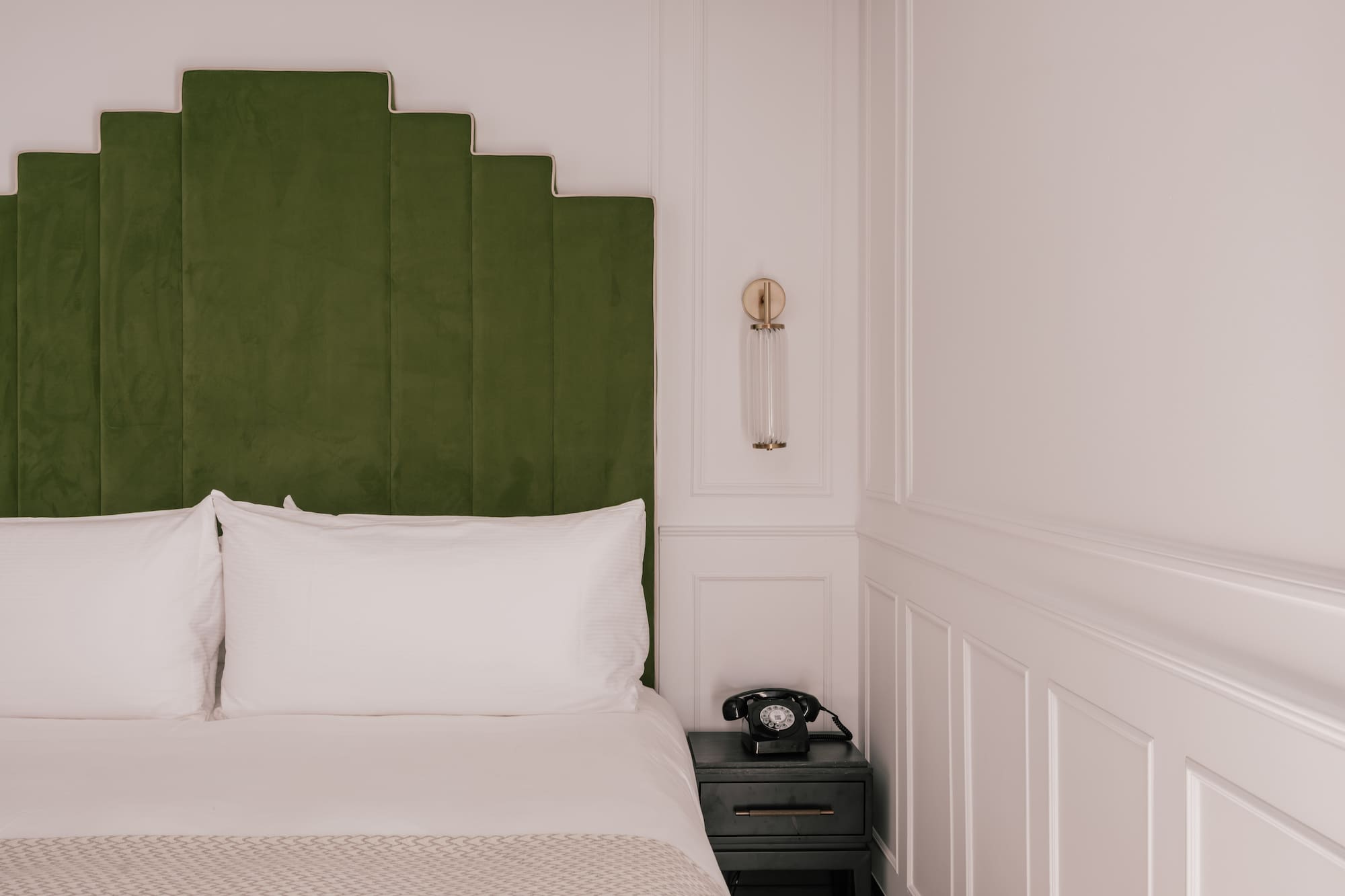 Green velvet geometric headboard, white bed, vintage phone, modern hotel room.