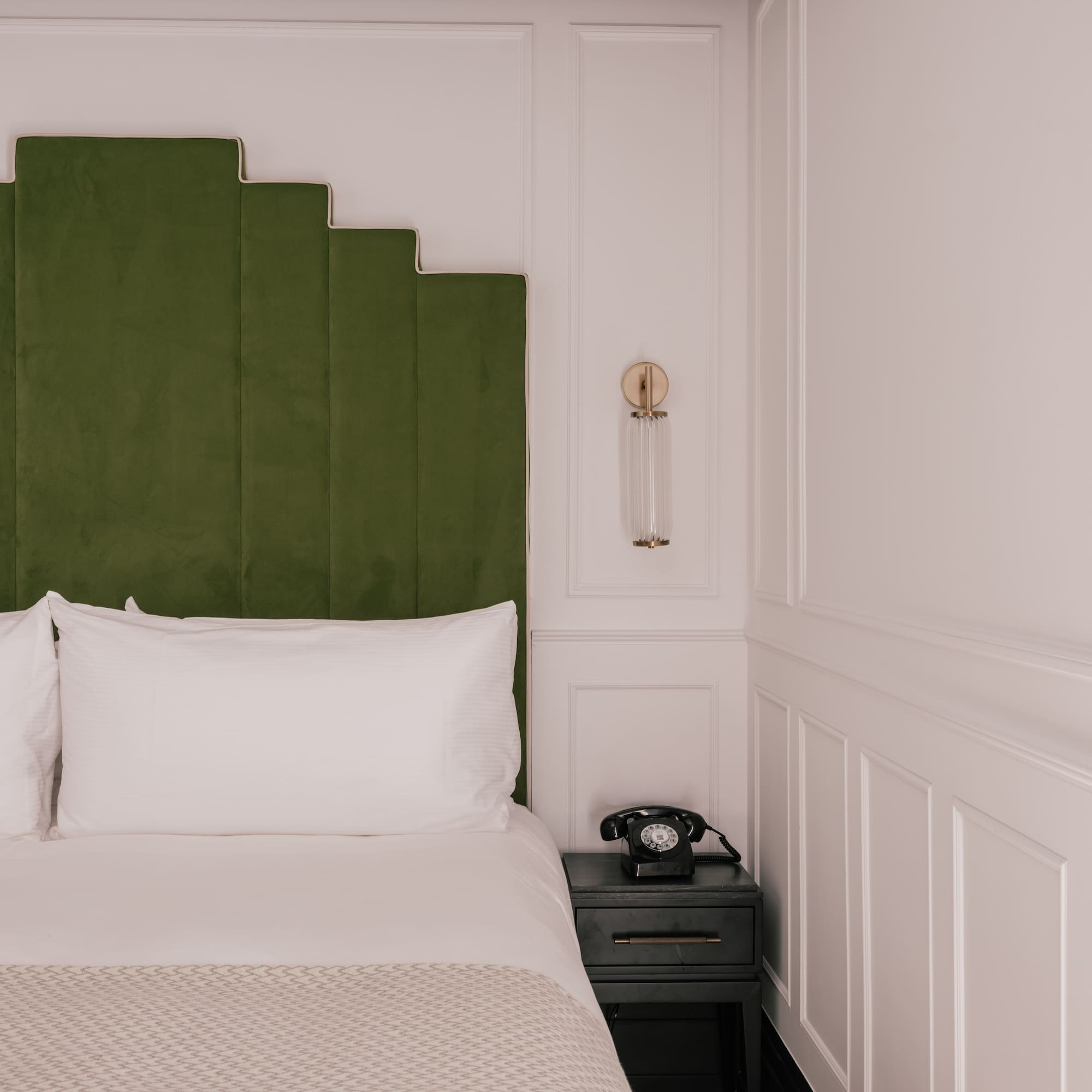 Green velvet geometric headboard, white bed, vintage phone, modern hotel room.