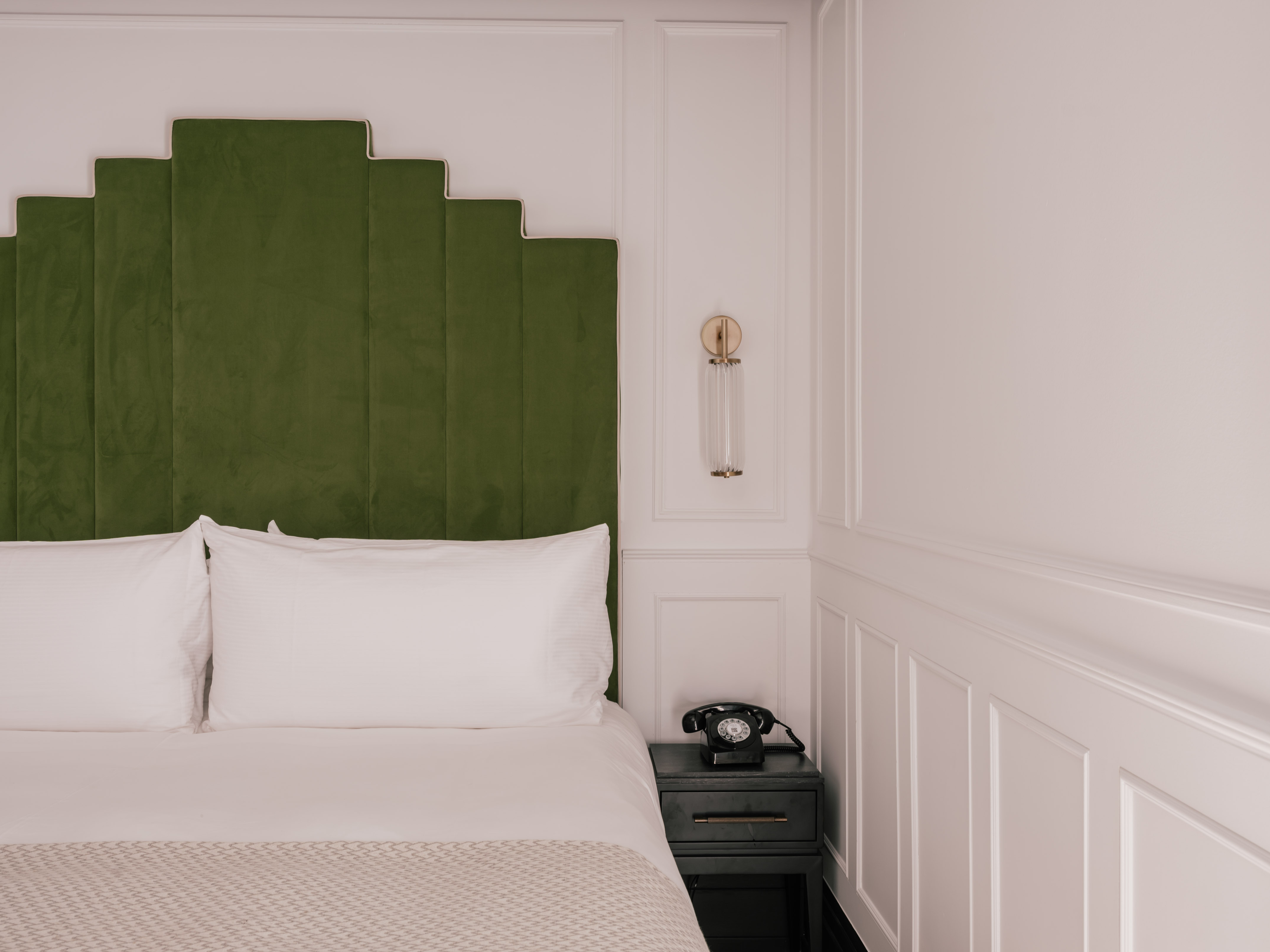 Green velvet geometric headboard, white bed, vintage phone, modern hotel room.