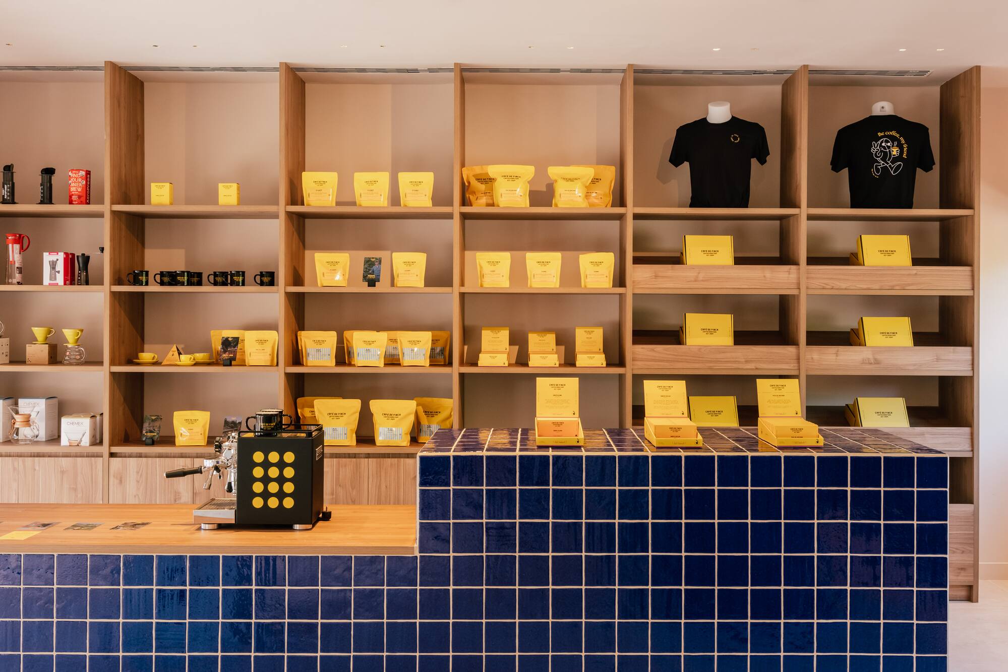Coffee shop with yellow packaged coffee, brewing gear, and blue tiled counter.