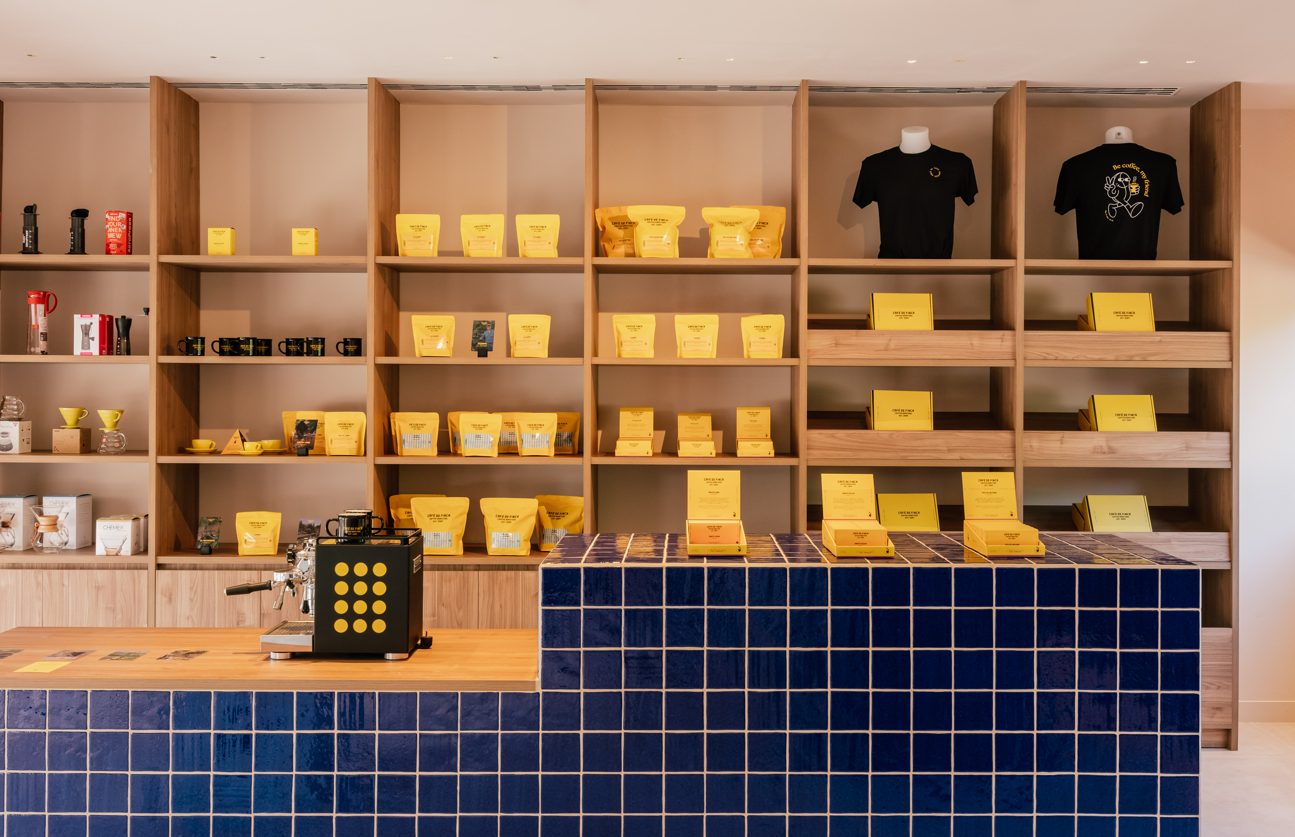 Coffee shop with yellow packaged coffee, brewing gear, and blue tiled counter.