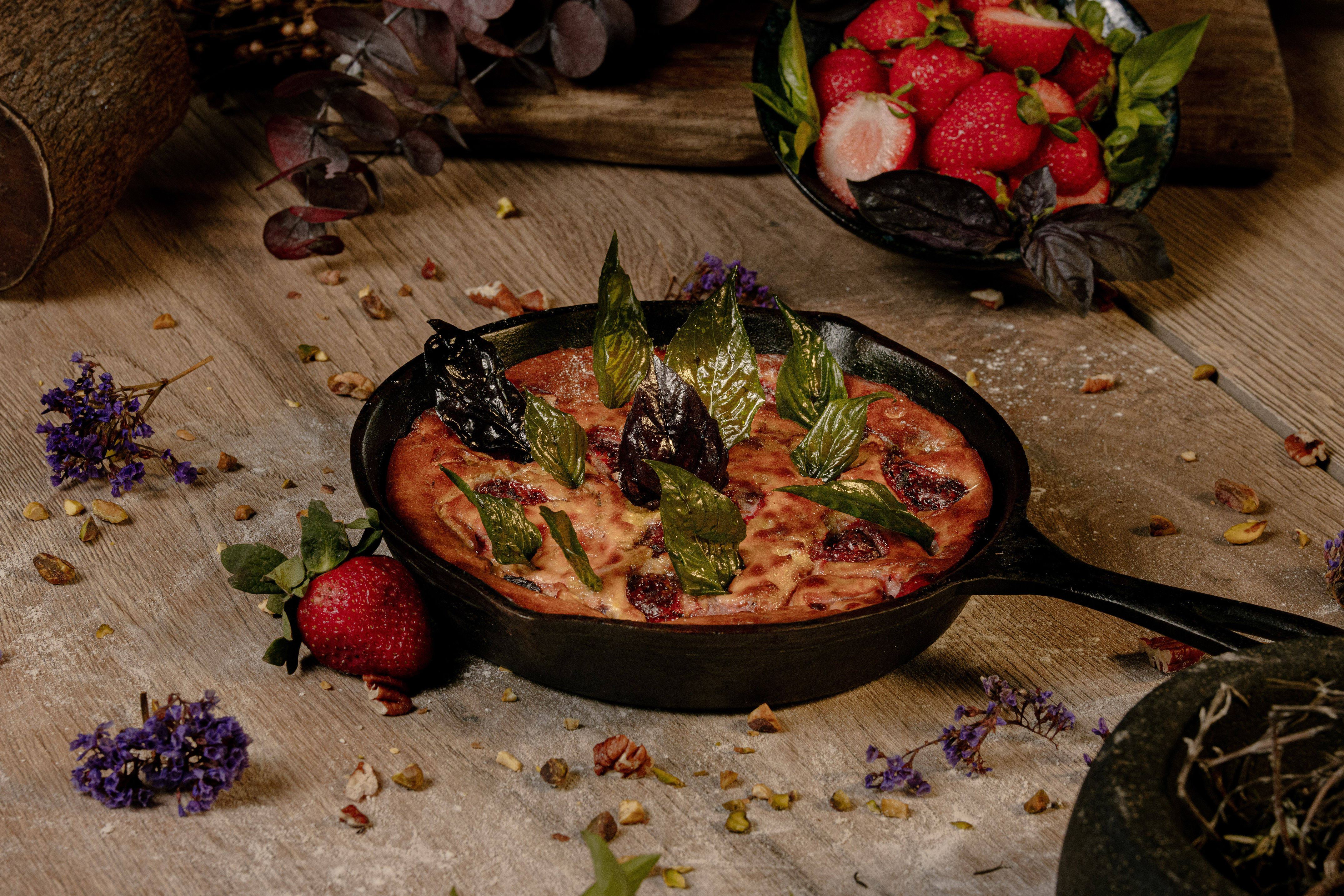 Baked strawberry tart in cast iron skillet, basil, fresh berries, rustic wood.