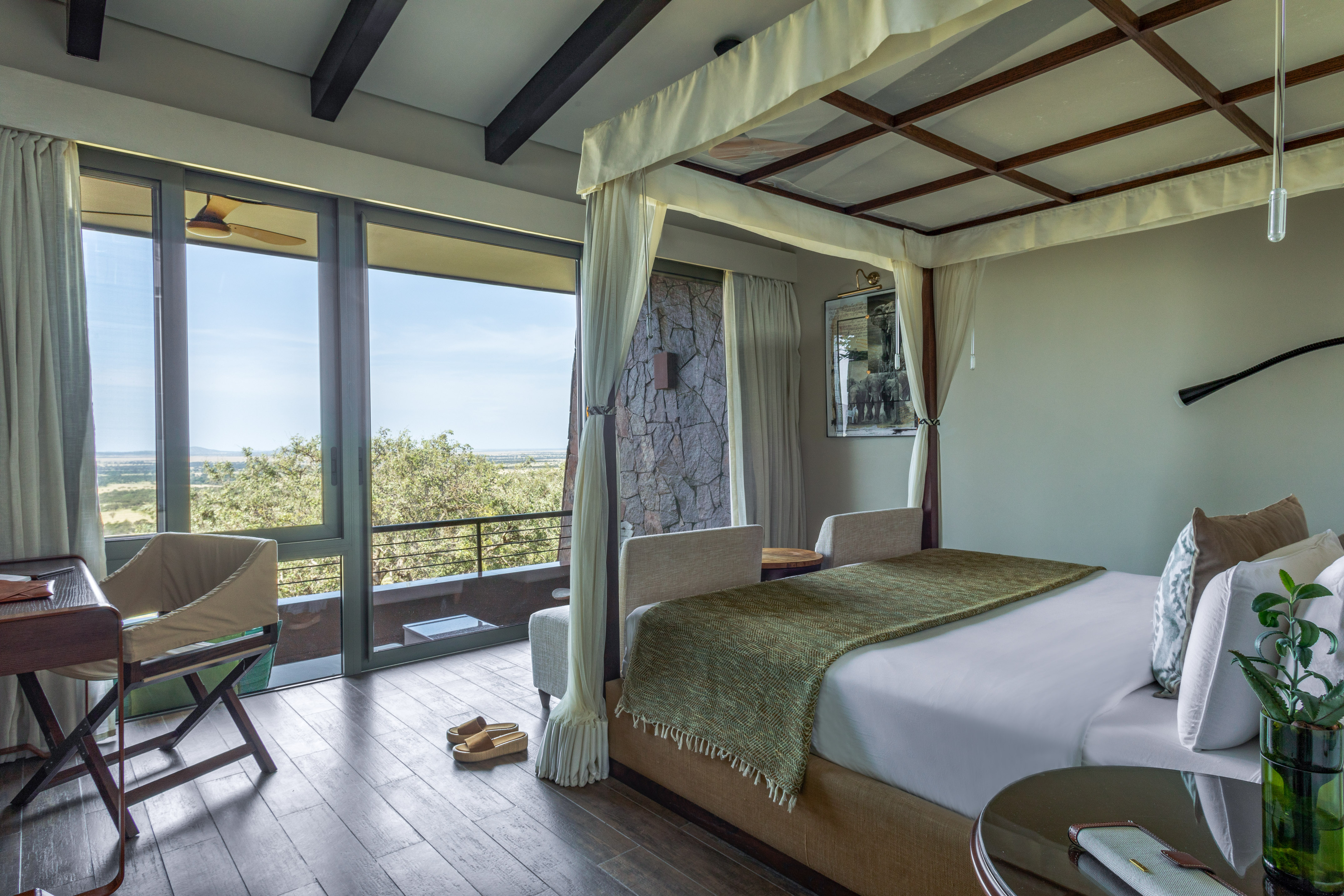 Luxury safari lodge bedroom with four-poster bed and panoramic savanna view.