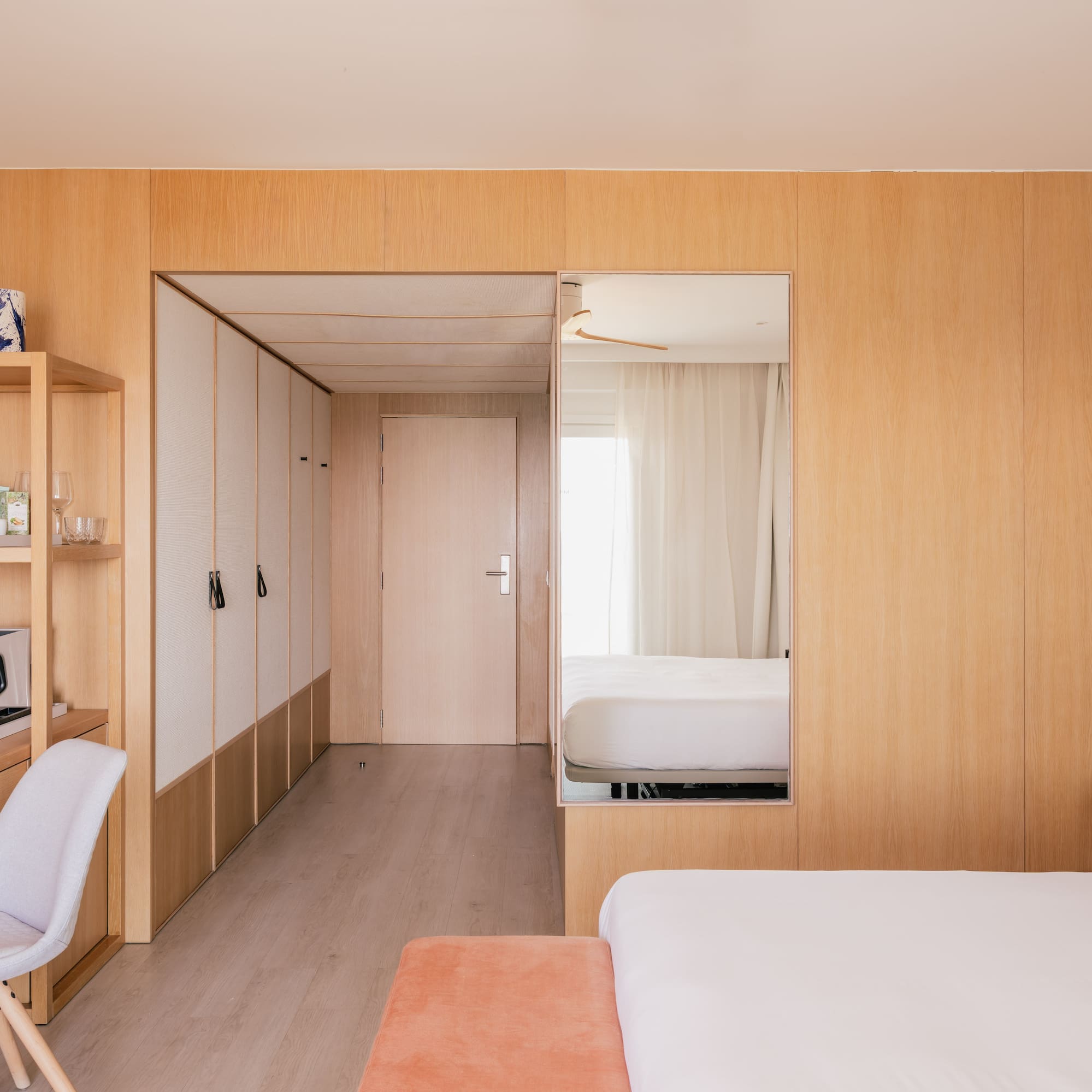Modern hotel room with wooden walls, desk, white bed, and large mirror.