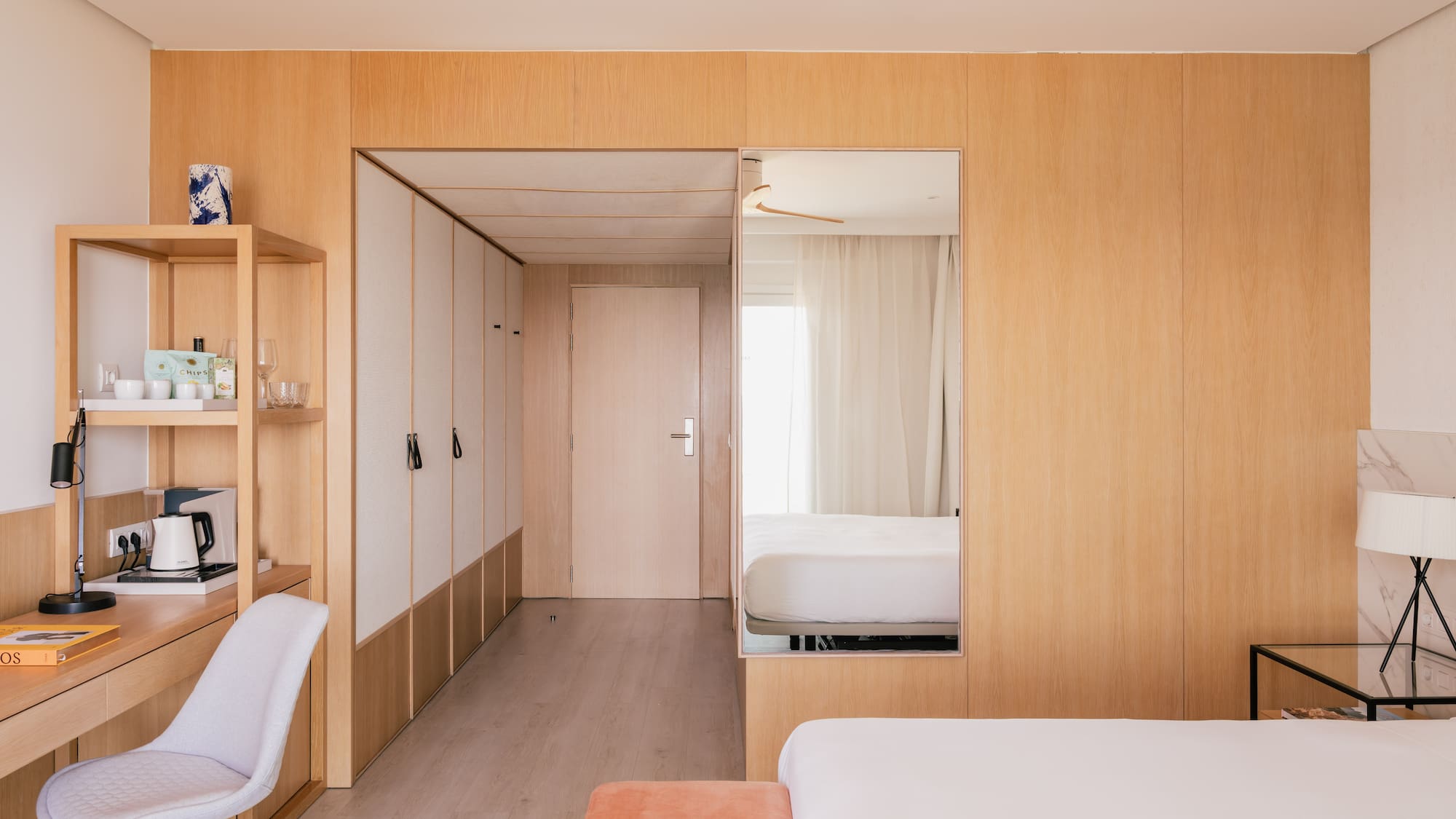 Modern hotel room with wooden walls, desk, white bed, and large mirror.