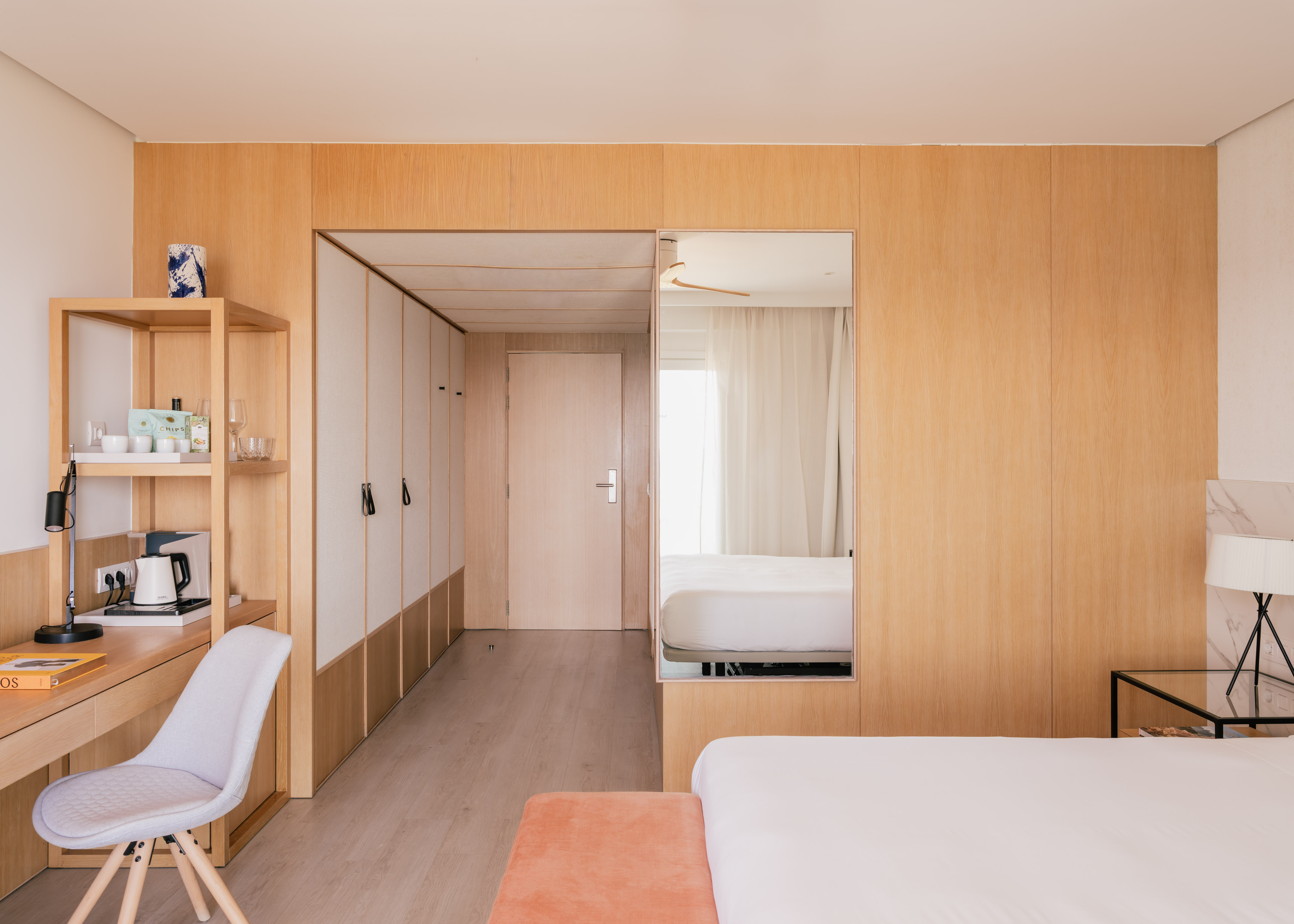 Dormitorio de hotel moderno con paneles de madera clara, escritorio y cama.