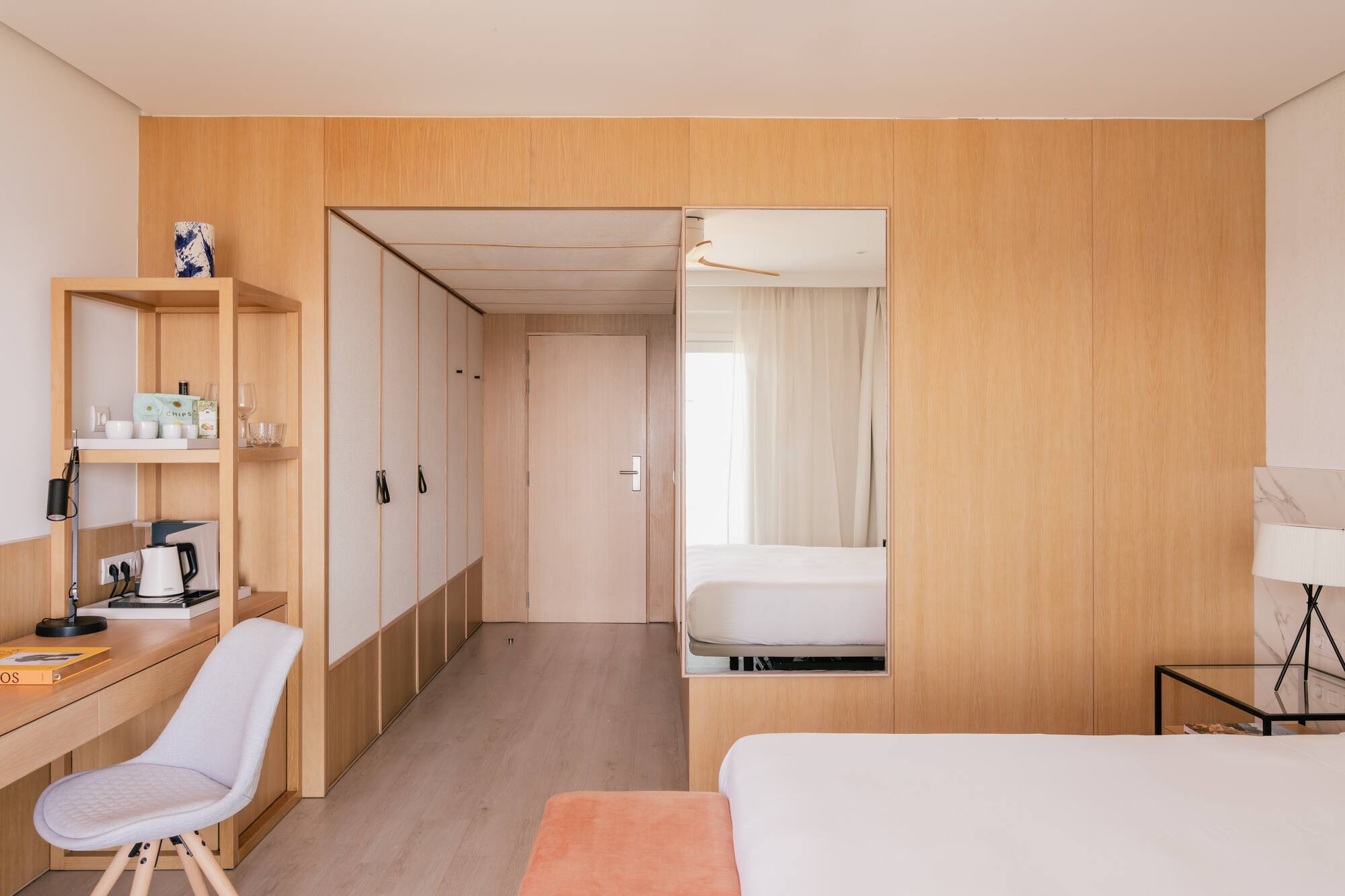 Dormitorio de hotel moderno con paneles de madera clara, escritorio y cama.