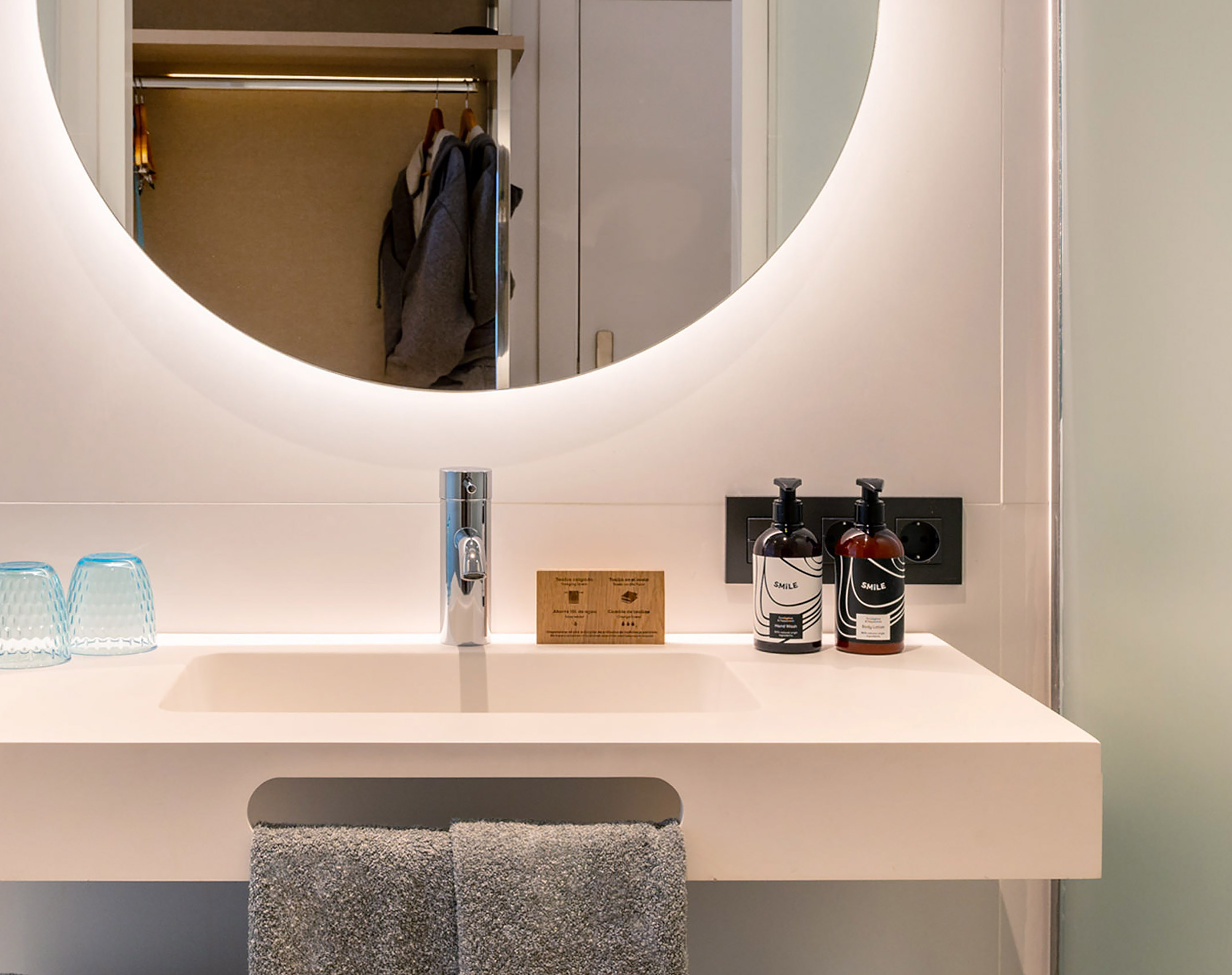 Modern hotel bathroom vanity with backlit mirror, sink, faucet, and toiletries.