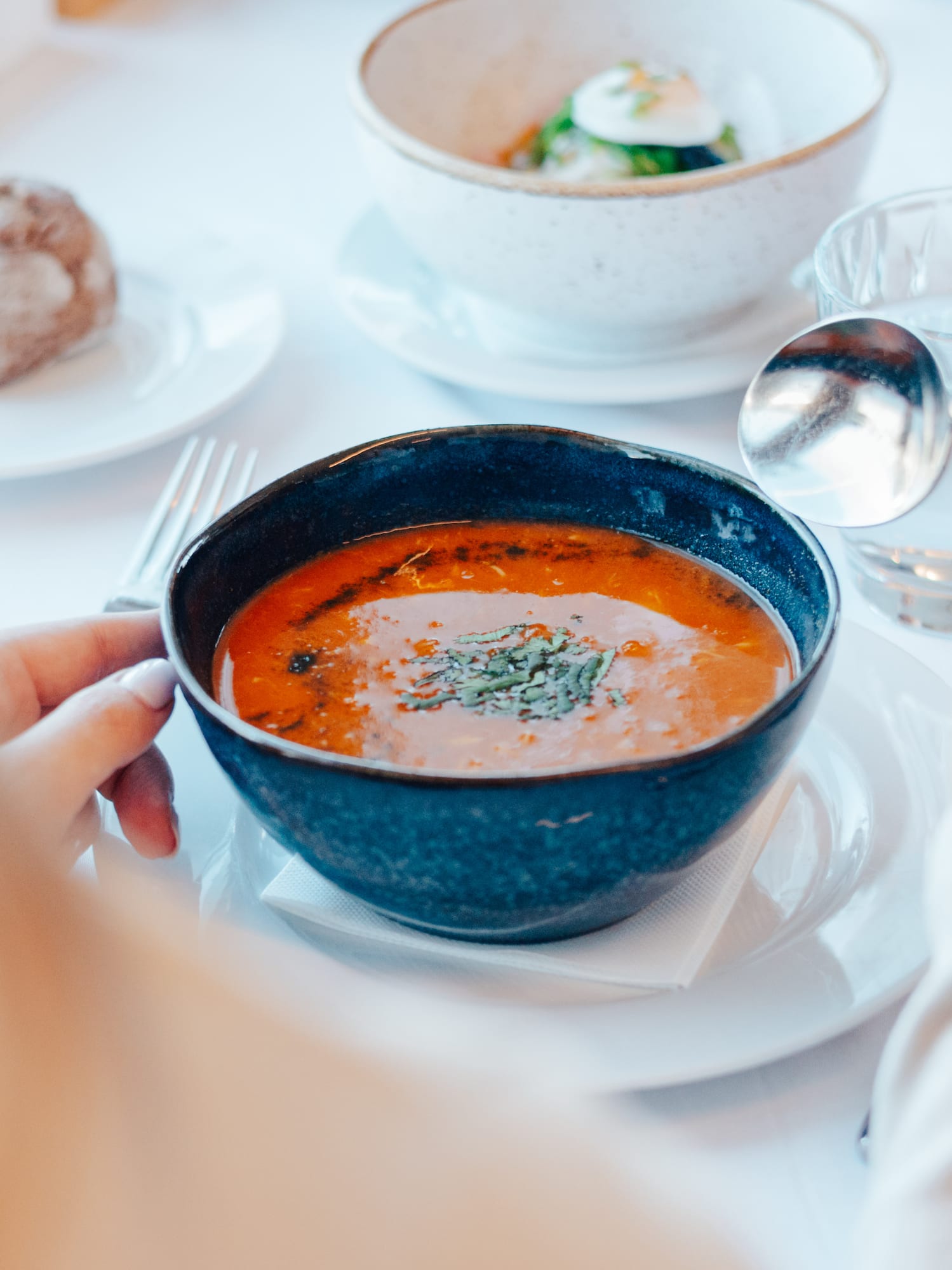 Person eating red soup with herbs, wine, and bread at a restaurant table.