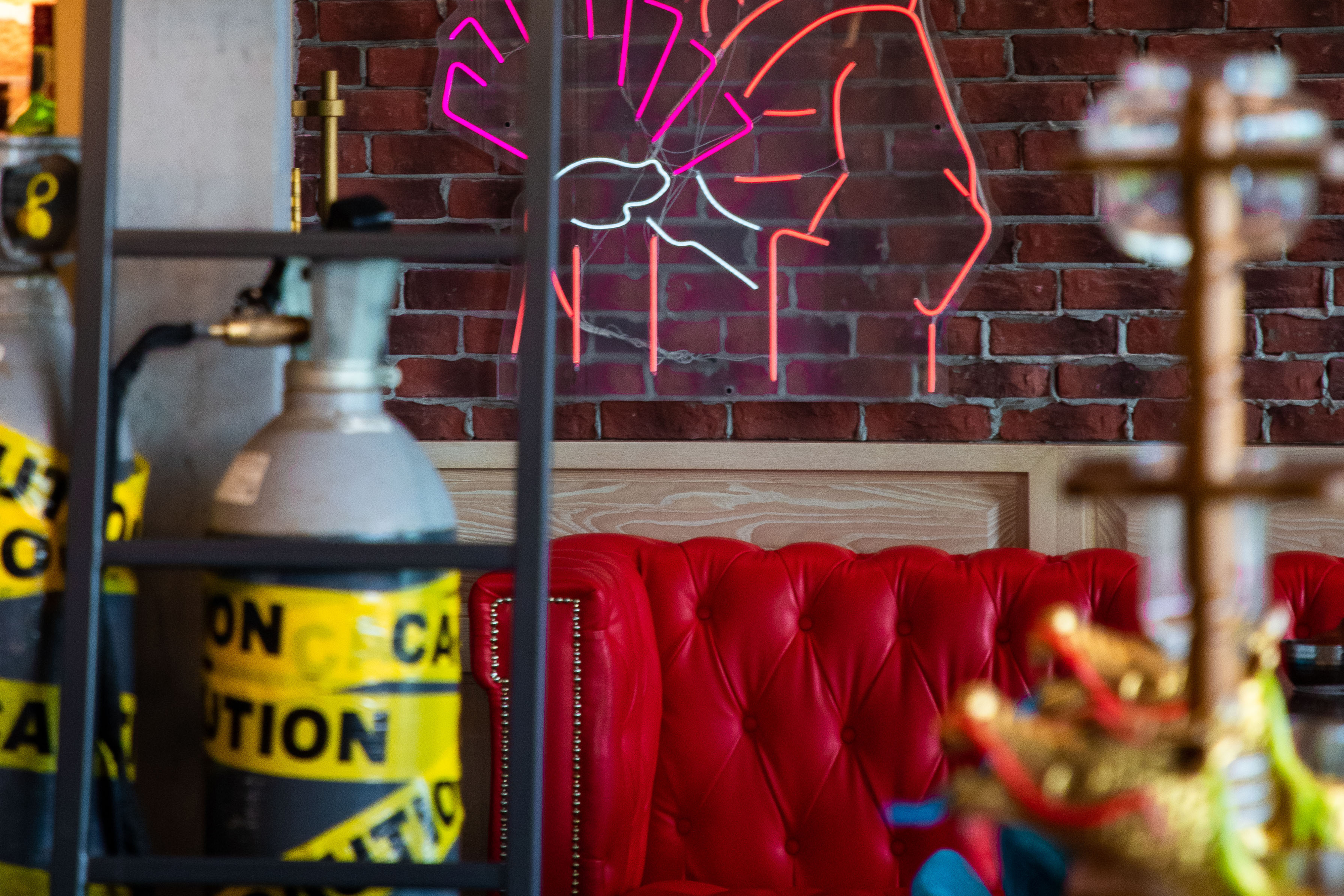 Red tufted leather couch, brick wall, neon fist sign, industrial bar decor.