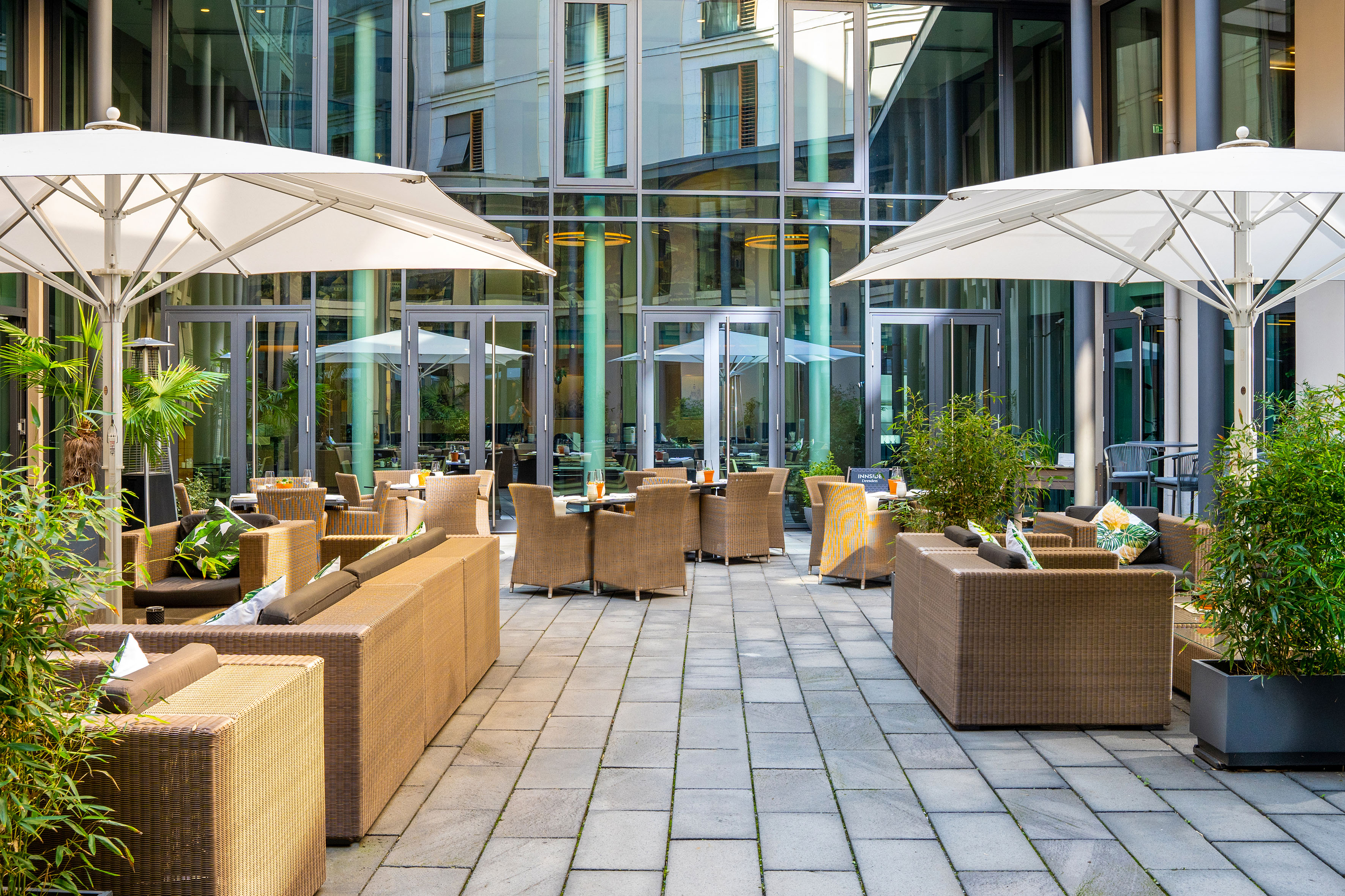 Outdoor hotel patio with rattan seating, white umbrellas, and modern glass building. - VEN Patio - Innside Dresda, Dresda