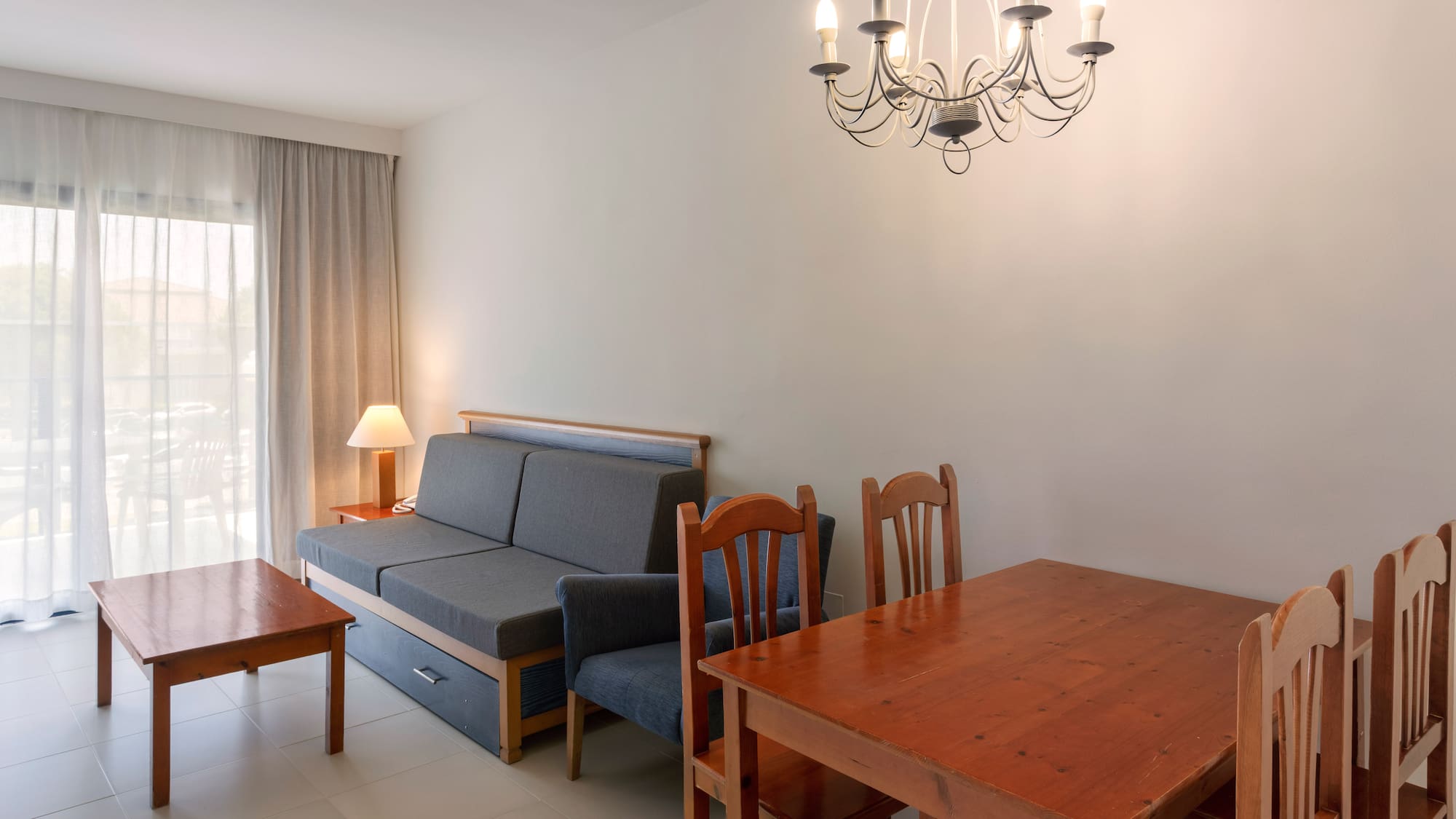 Bright living room with gray sofa bed, wooden dining table, coffee table, and chandelier.