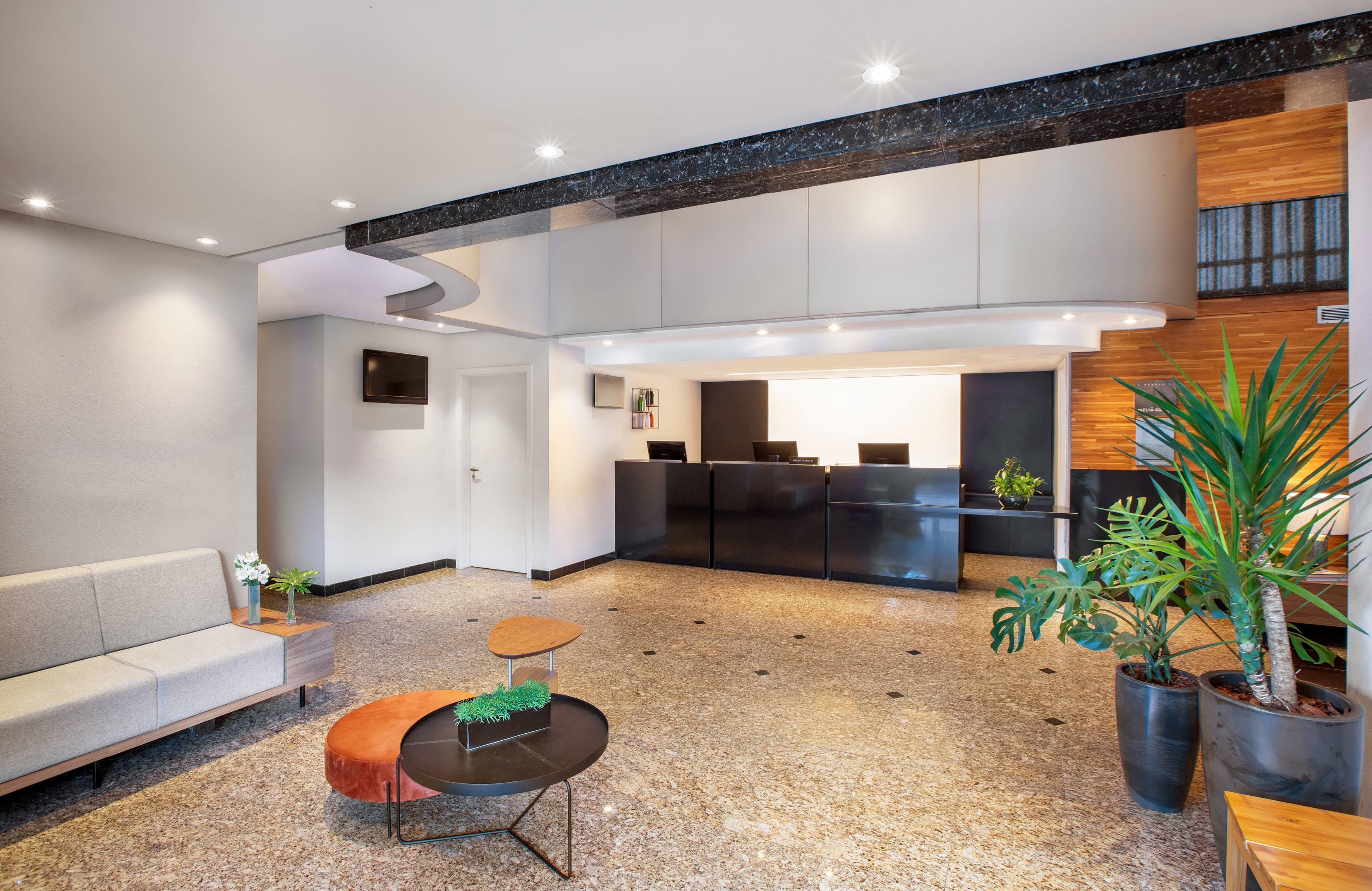 Modern hotel lobby with black reception desk, gray sofa, and plant decor.