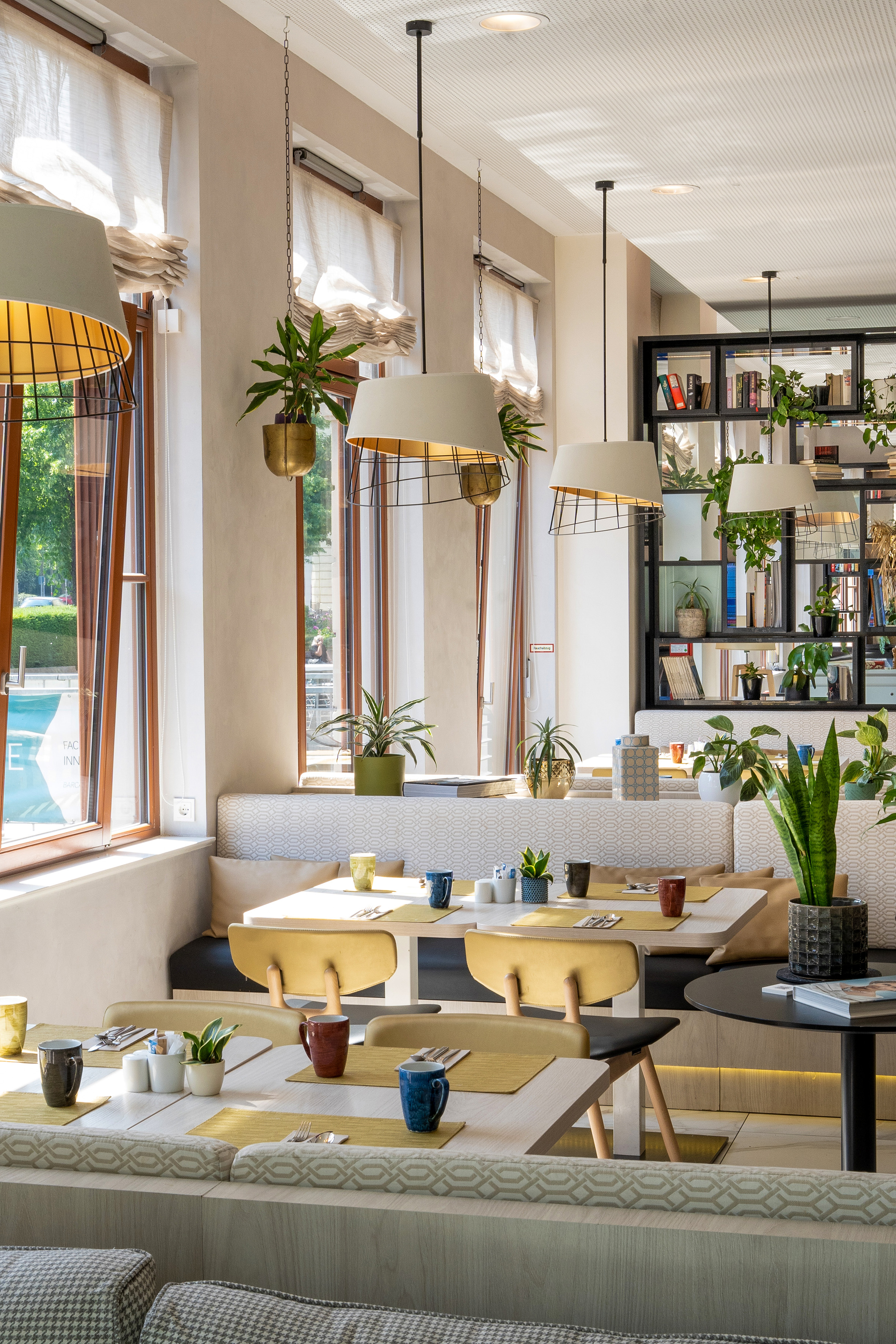 Bright modern cafe dining area with green plants and natural light.