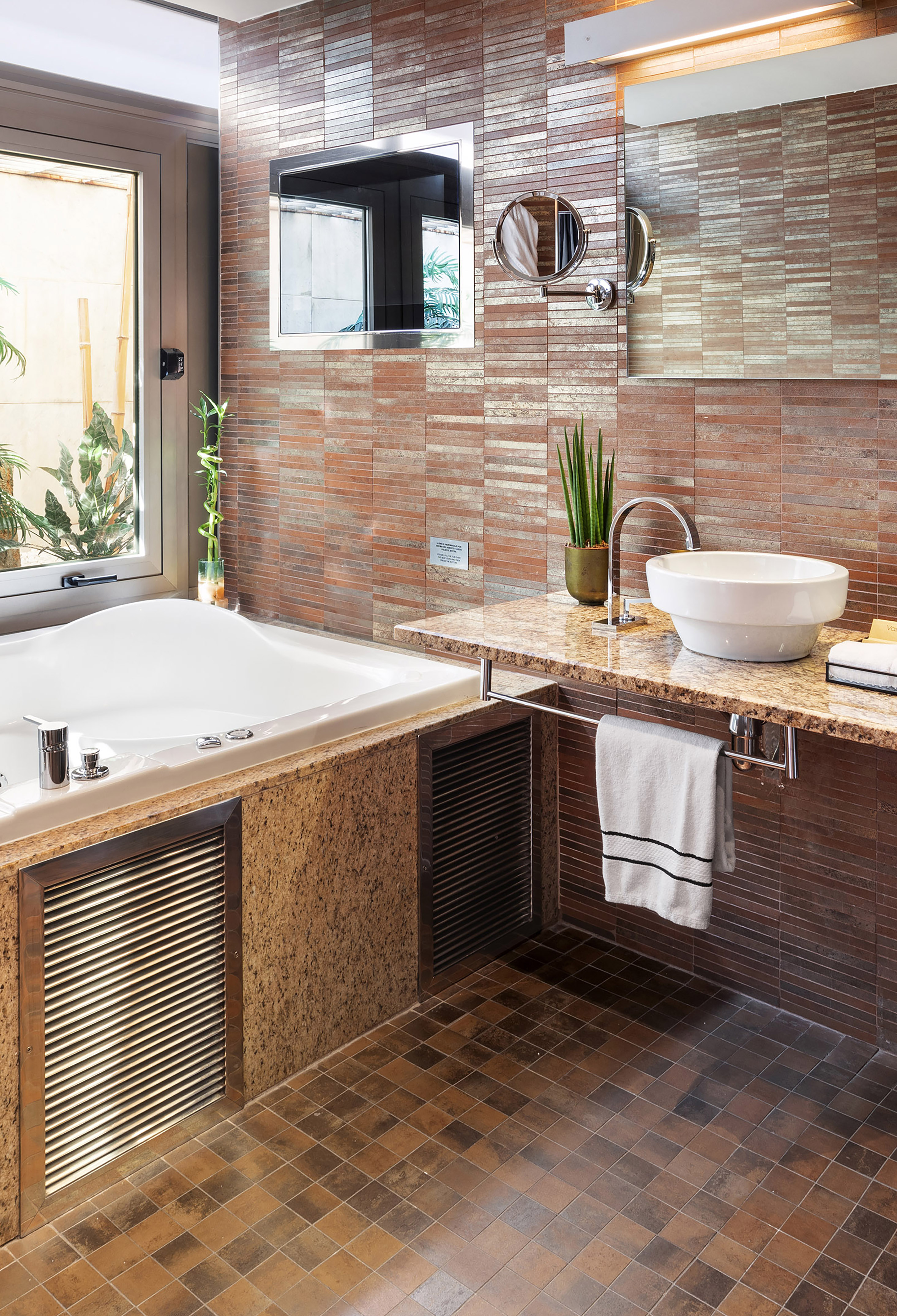 Modern bathroom with bathtub, window, granite vanity, vessel sink, and brown tiled walls.