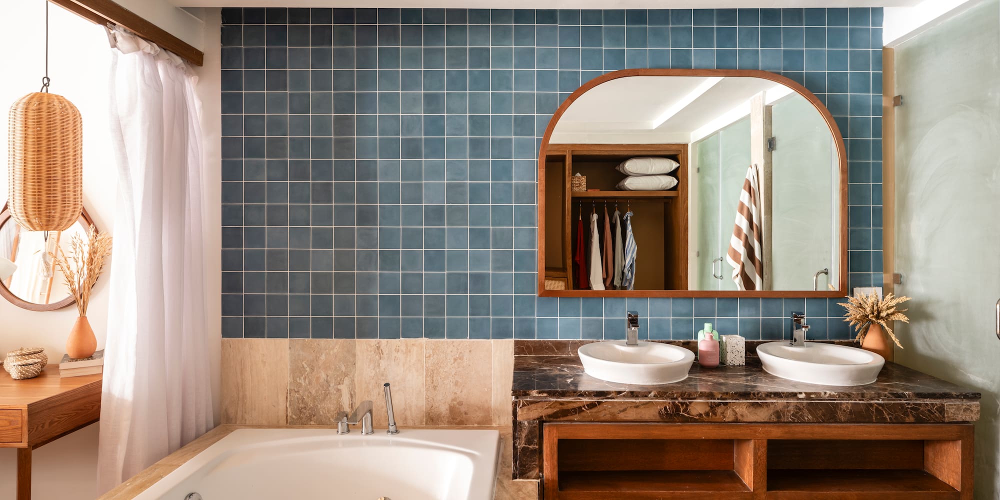 Blue tiled bathroom with double vanity, jetted tub, and arched mirror.
