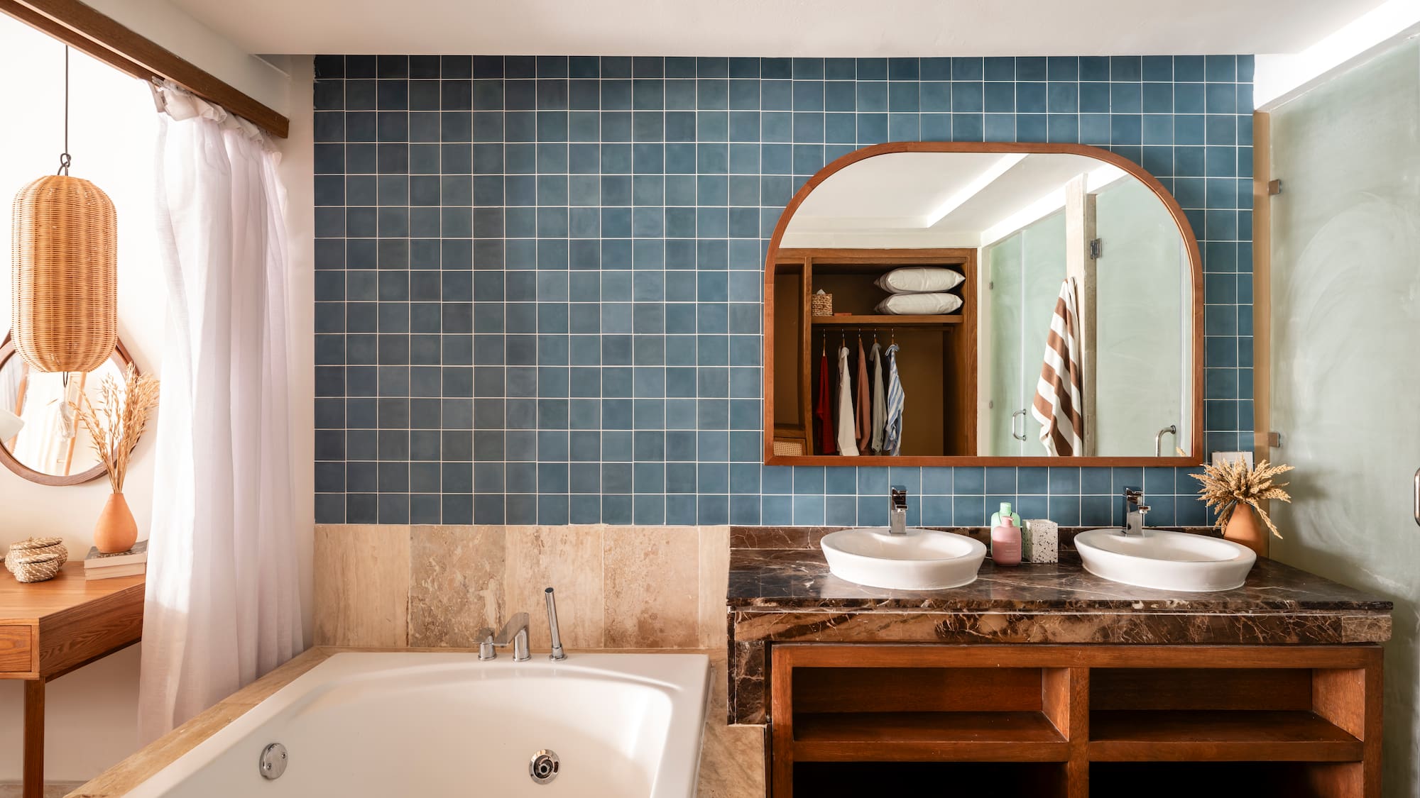 Blue tiled bathroom with double vanity, jetted tub, and arched mirror.