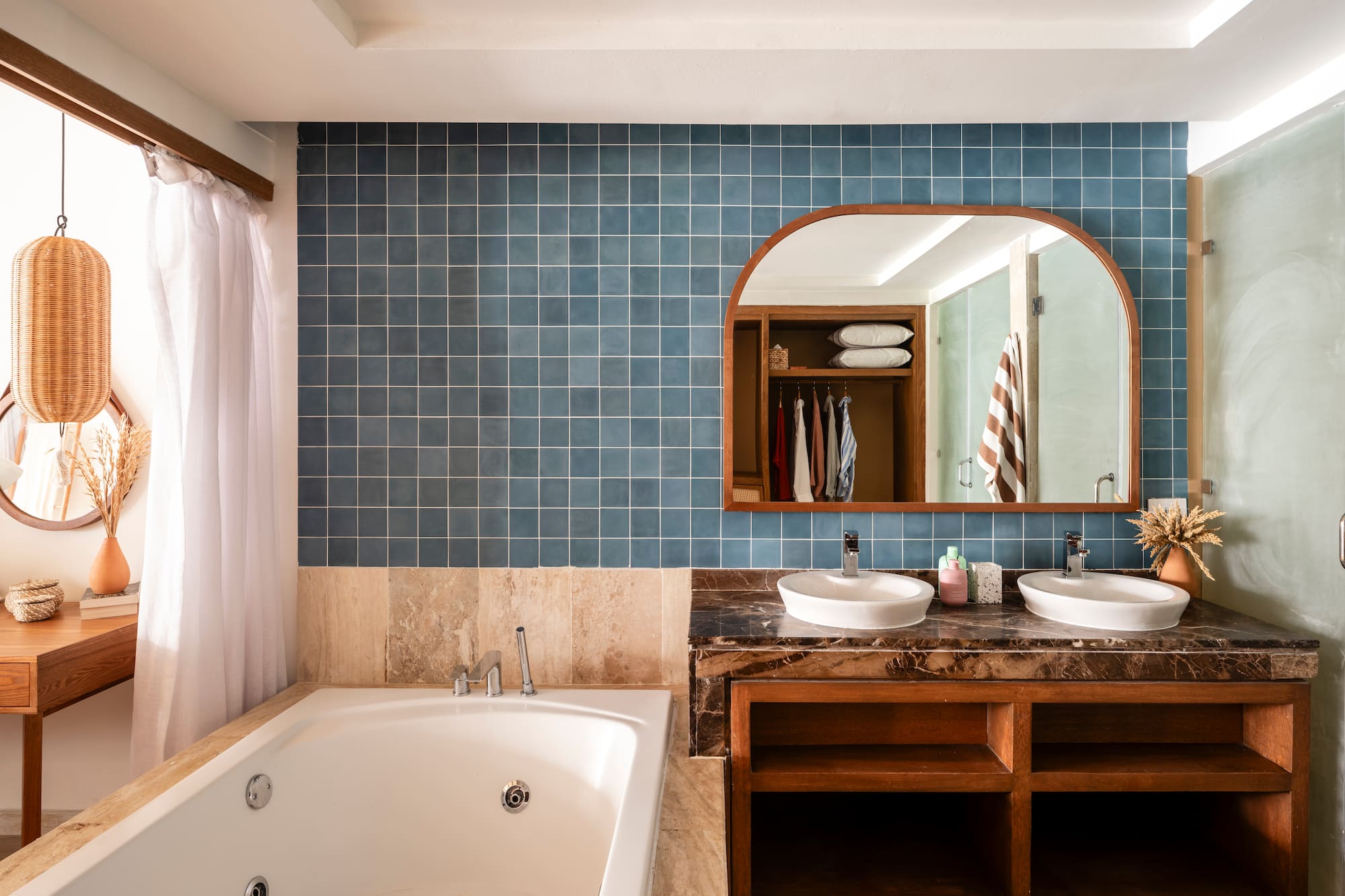 Blue tiled bathroom with double vanity, jetted tub, and arched mirror.
