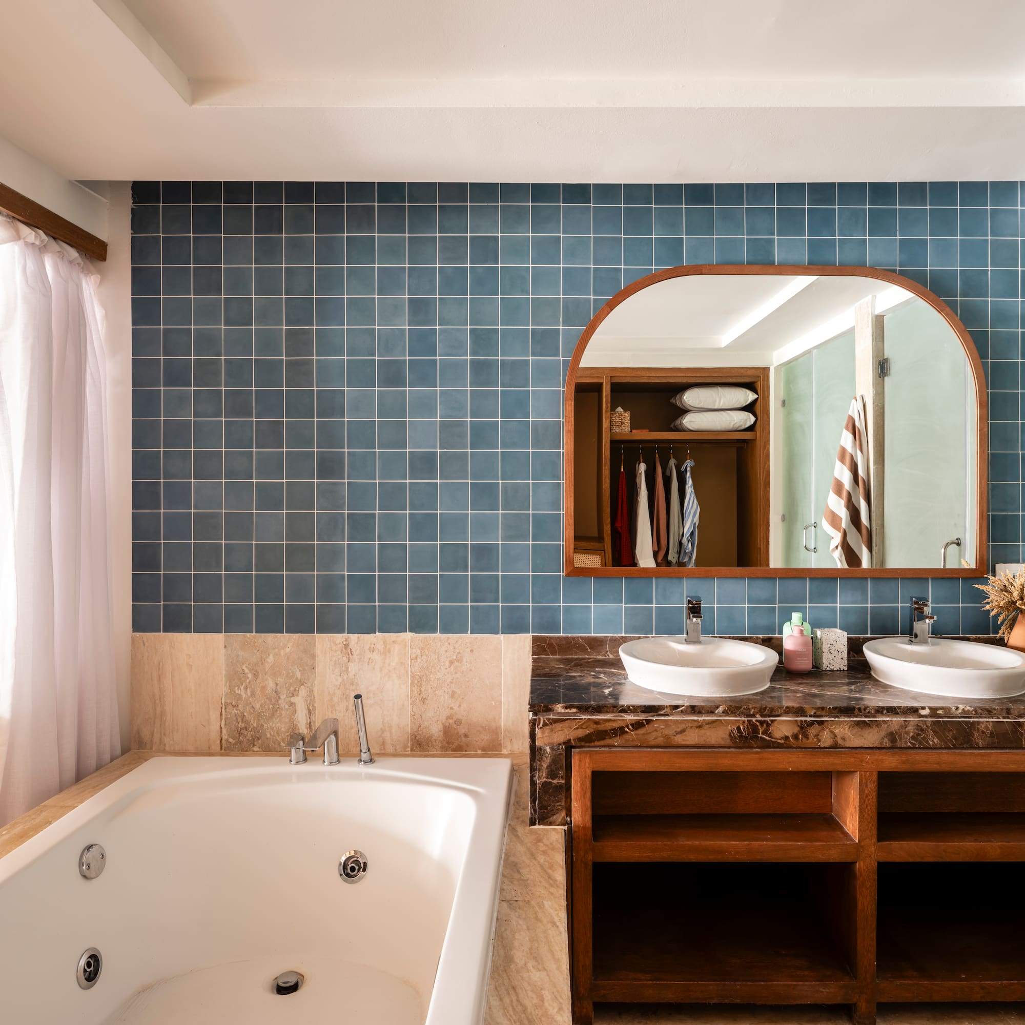 Blue tiled bathroom with double vanity, jetted tub, and arched mirror.