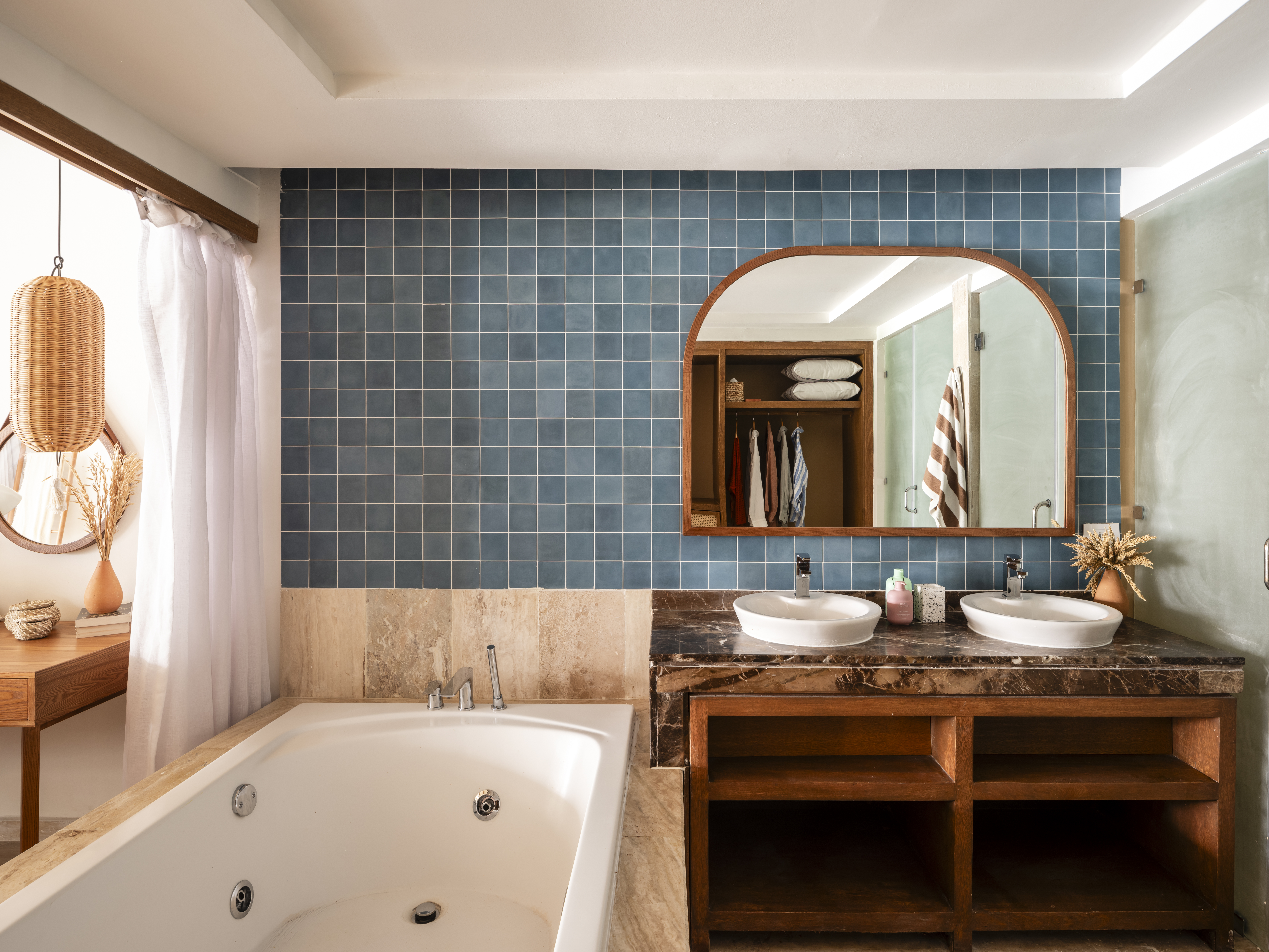 Blue tiled bathroom with double vanity, jetted tub, and arched mirror.