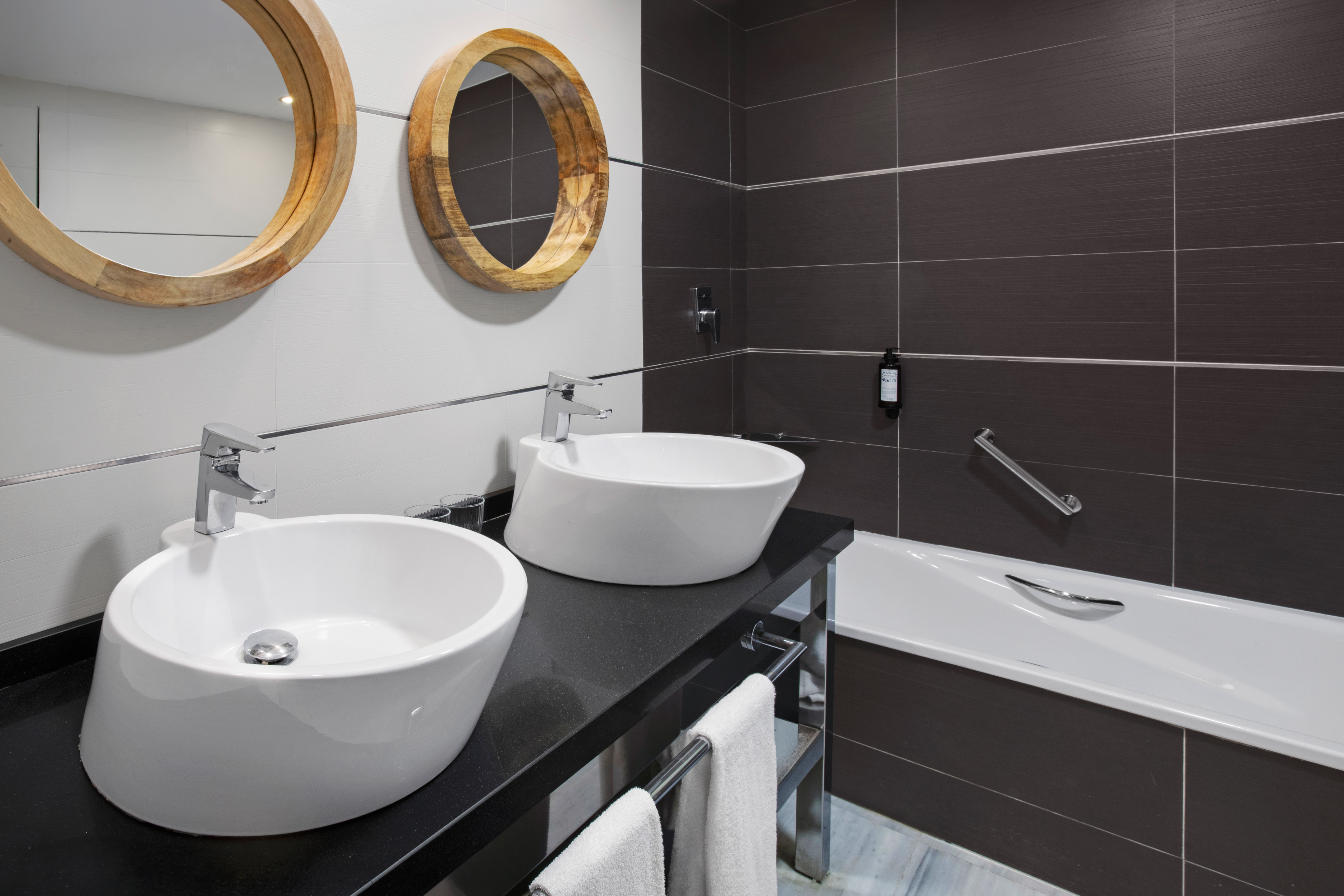 Modern bathroom with two vessel sinks, round wooden mirrors, and bathtub.