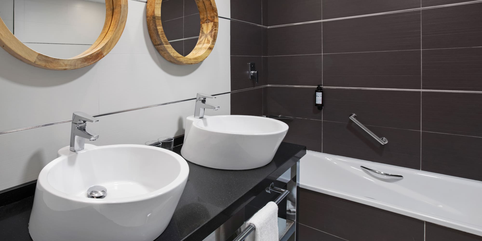 Modern bathroom with two vessel sinks, round wooden mirrors, and bathtub.