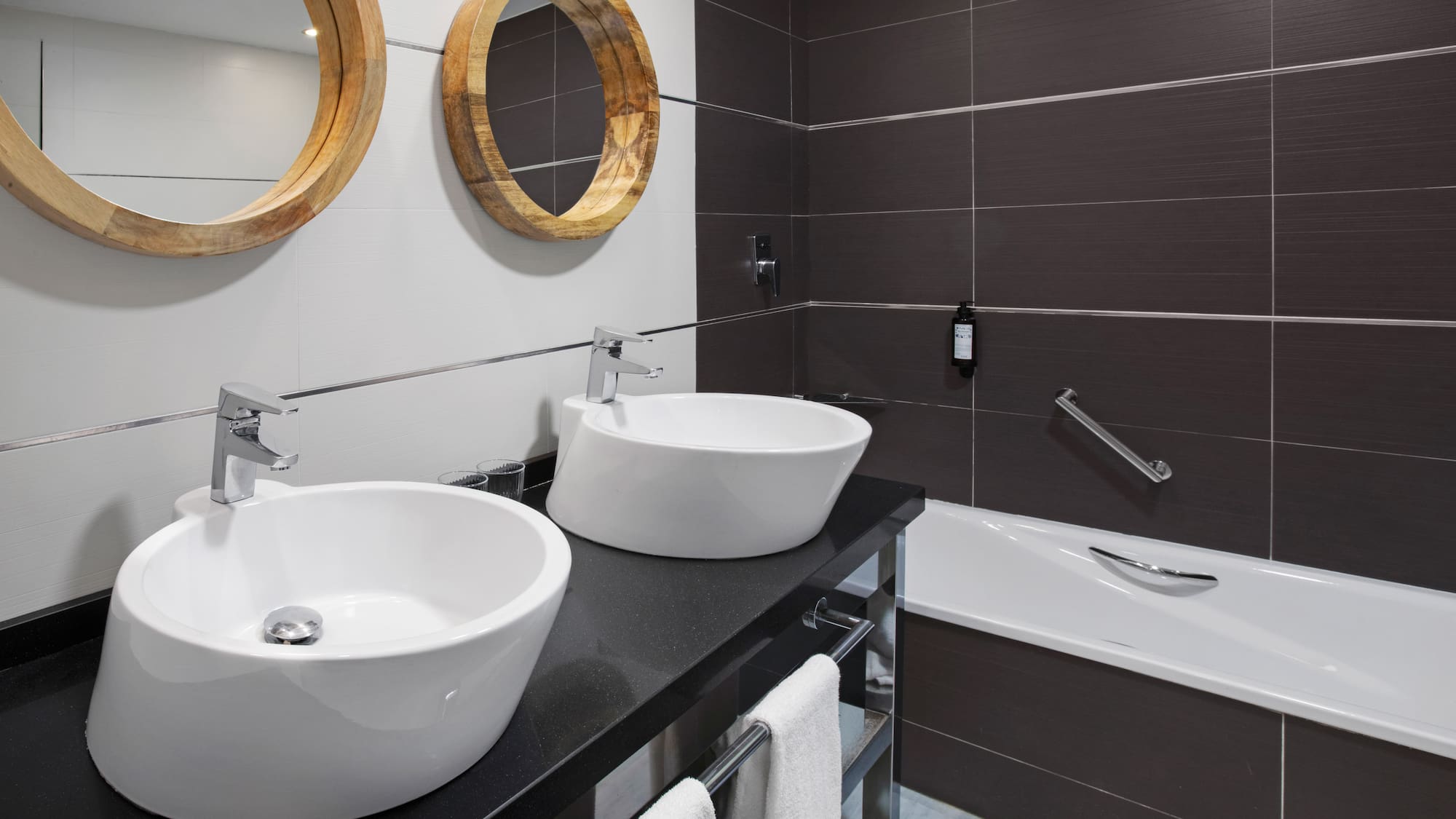 Modern bathroom with two vessel sinks, round wooden mirrors, and bathtub.